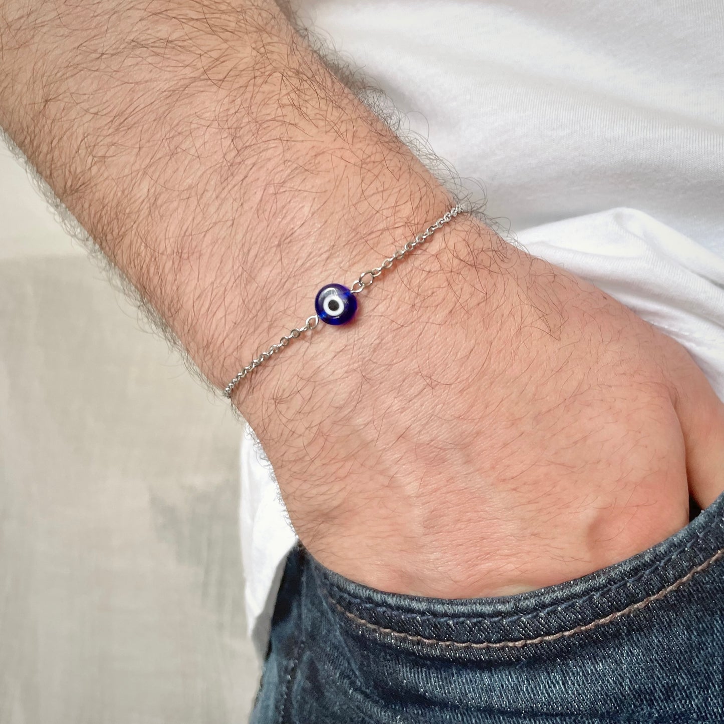 Close-up of a men's wrist wearing a silver bracelet with an evil eye charm.