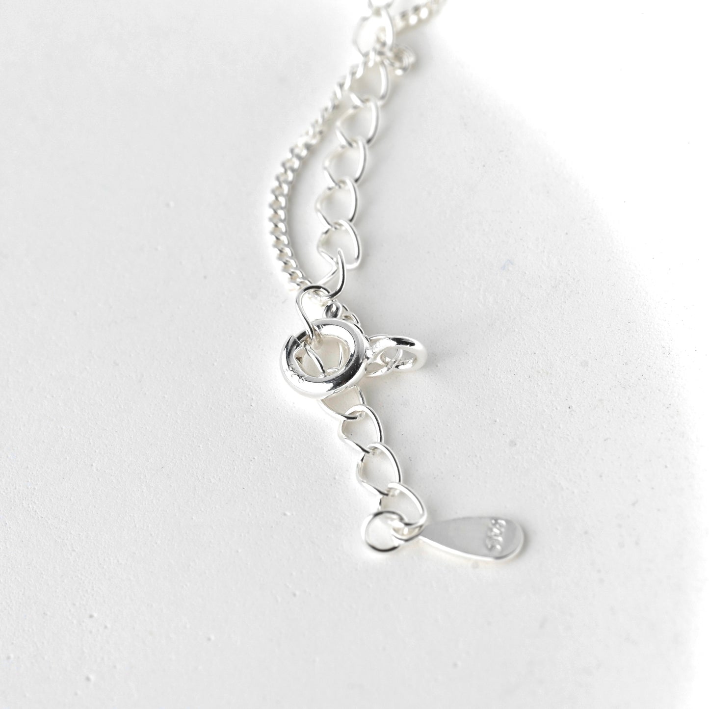 Close-up view of the silver necklace with a spring ring clasp and tag with S925 stamp on a white background