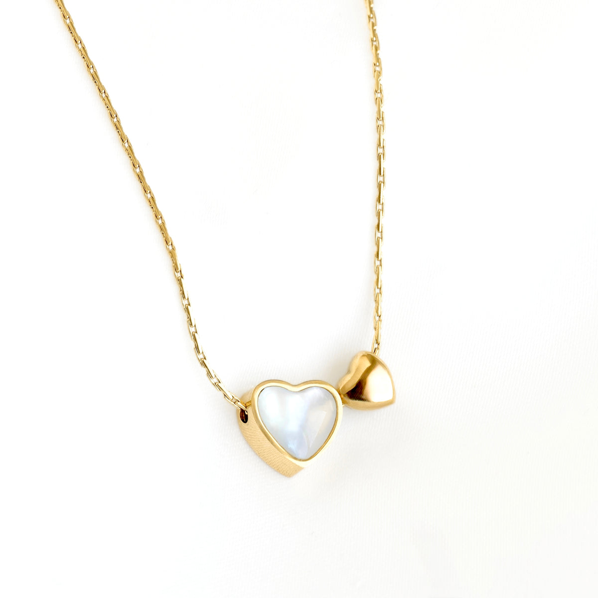 A delicate gold chain necklace featuring a small heart-shaped pendant with a white iridescent inlay and a second small gold heart beside it, shown on a plain white background.