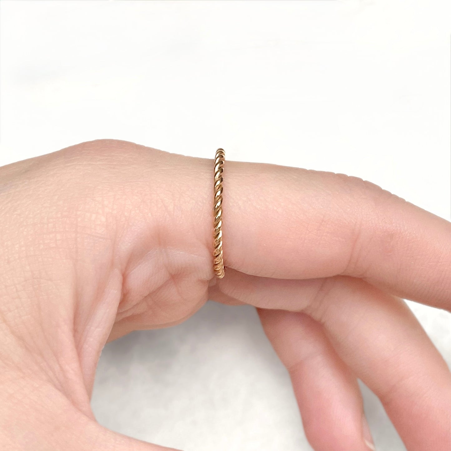 Side view of index finger wearing a twisted gold ring against a white background