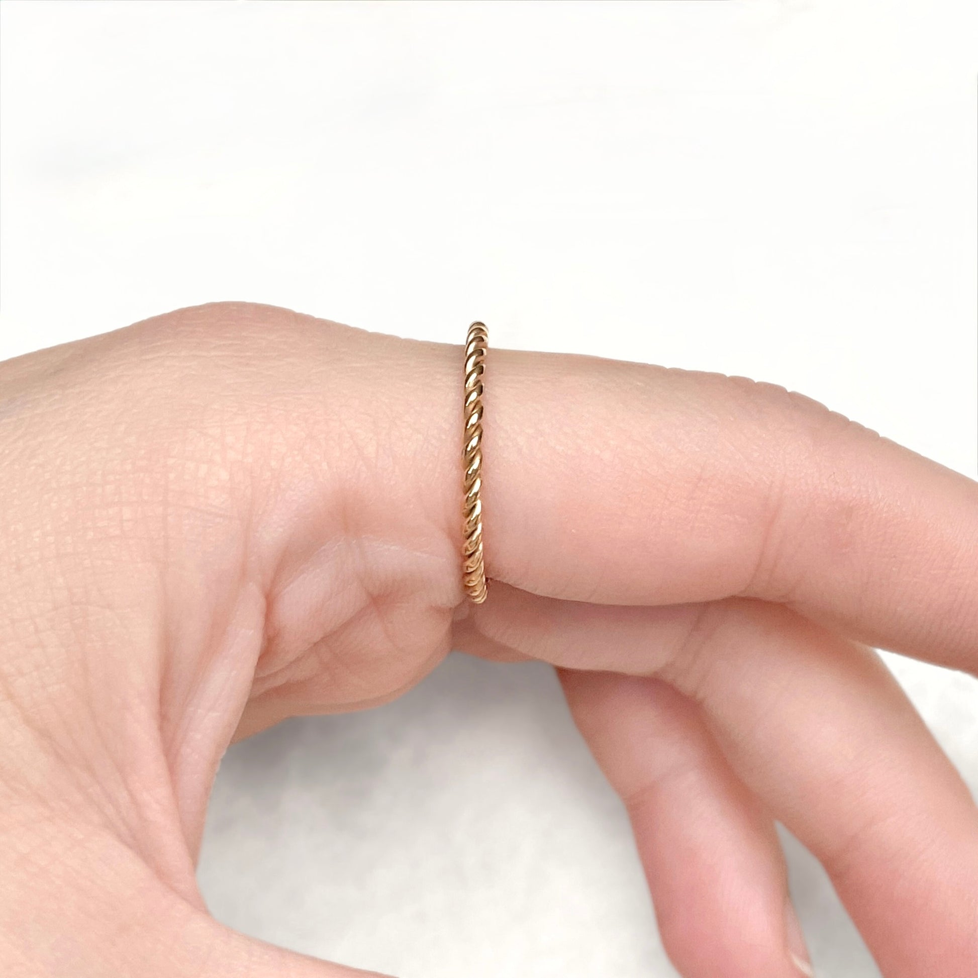 Side view of index finger wearing a twisted gold ring against a white background