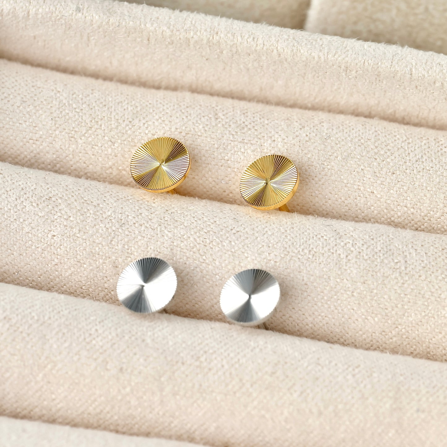 Gold and silver round textured earrings on a textured beige surface