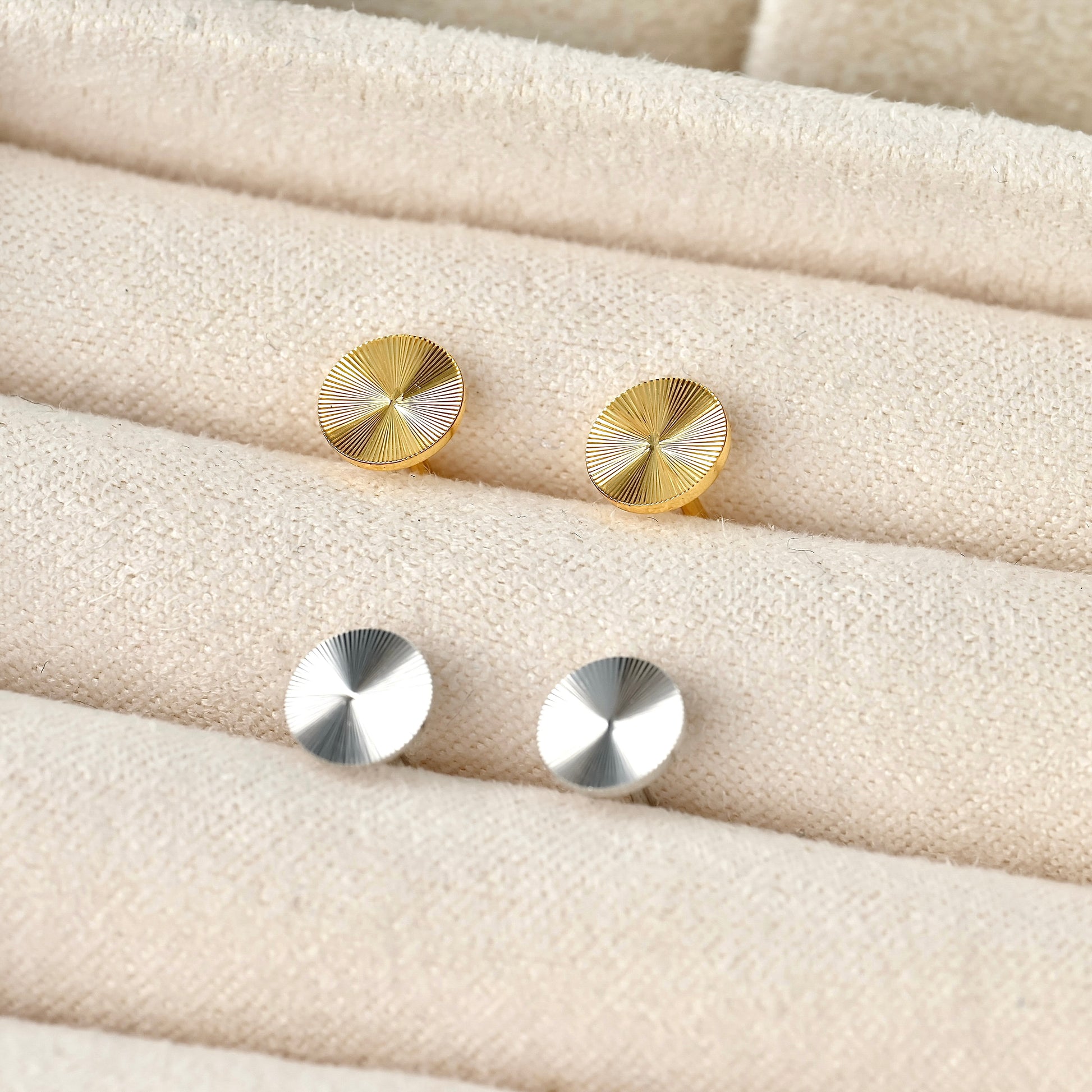 Gold and silver round textured earrings on a textured beige surface