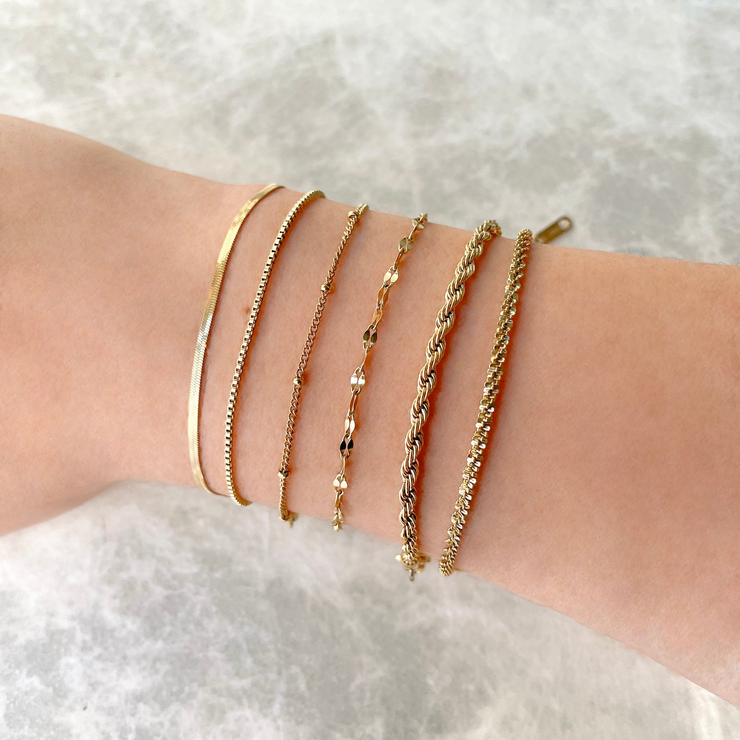 Six gold chain bracelets on a person's wrist against a white background