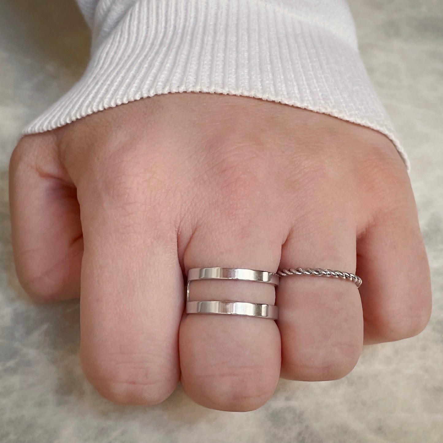 Top view of hand wearing stacked illusion silver ring on a neutral background