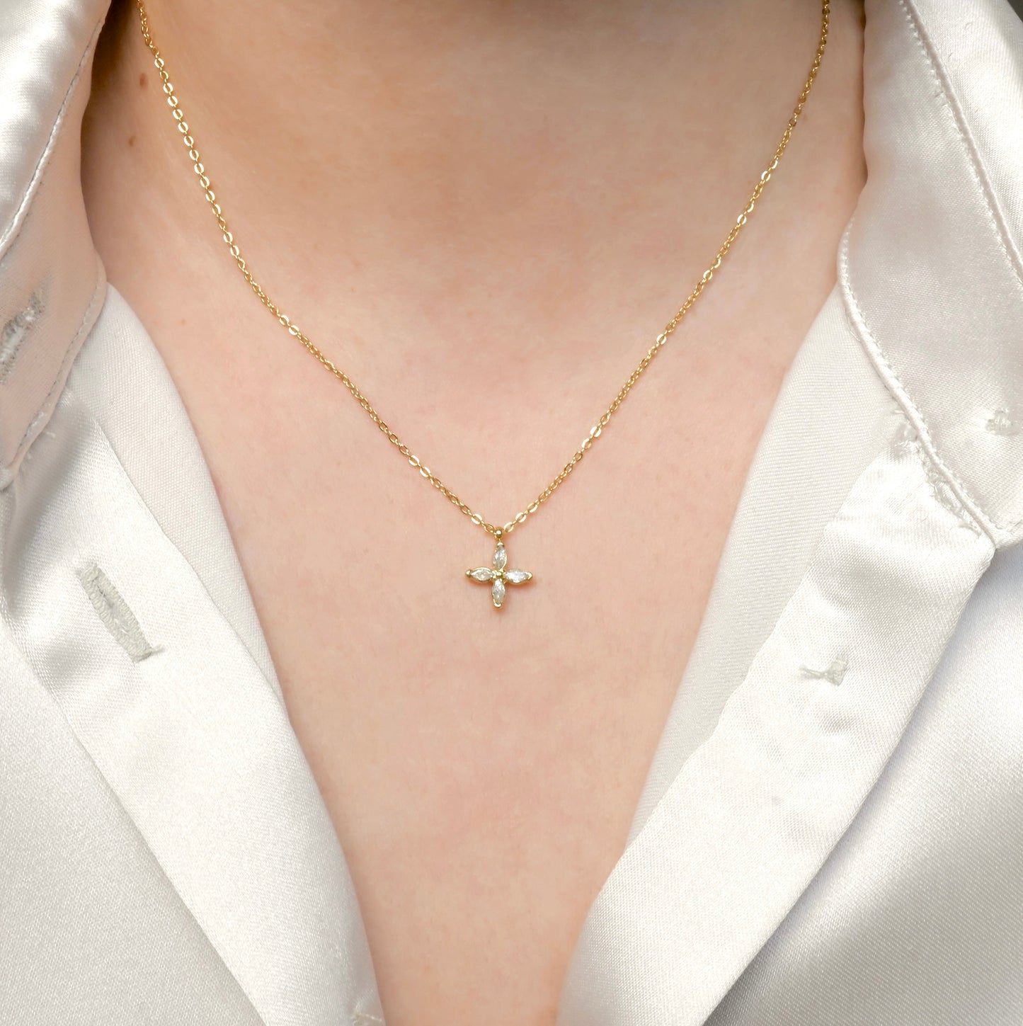 Gold necklace with a floral pendant worn by a person in a white blazer.