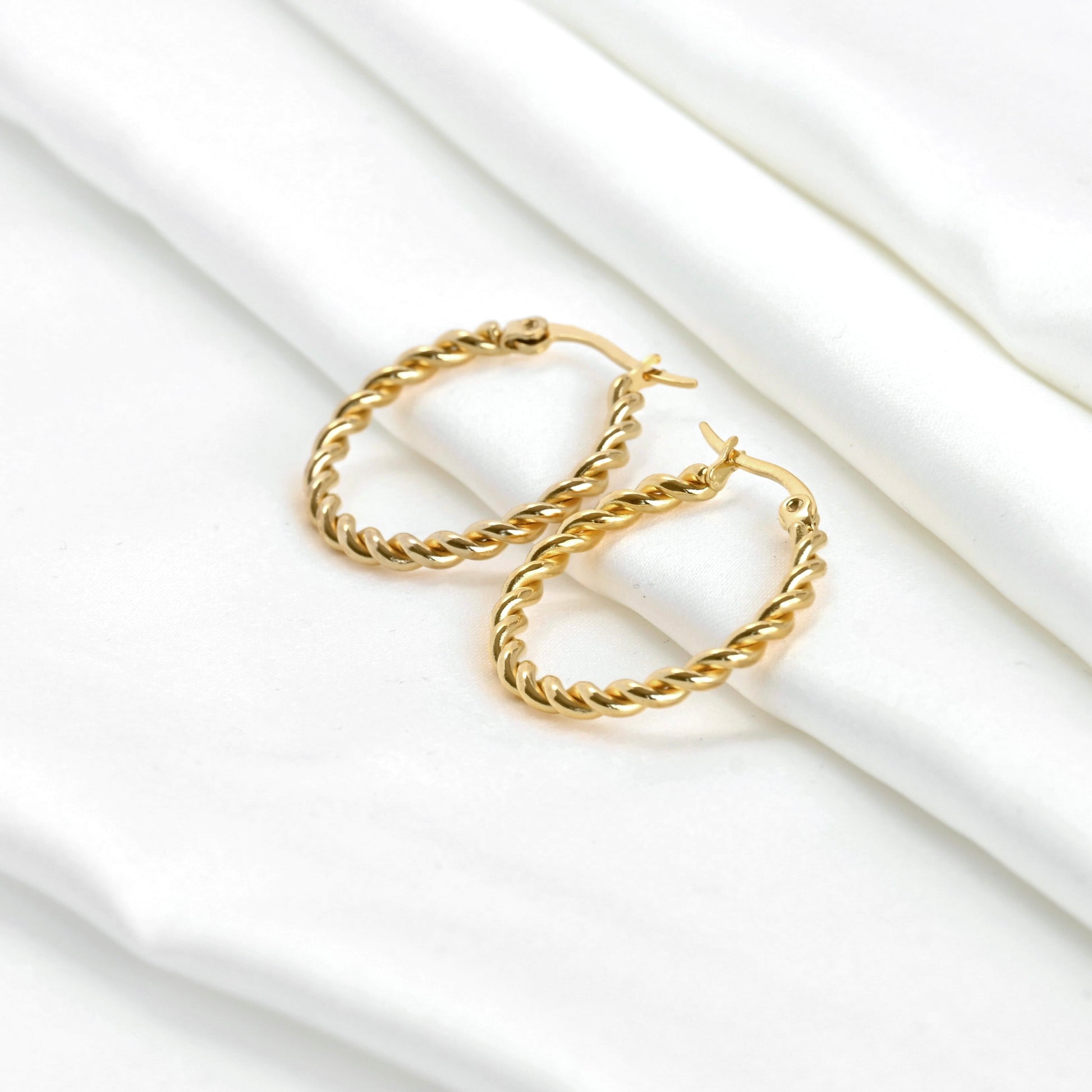 Gold thin twisted hoop earrings on a white fabric background