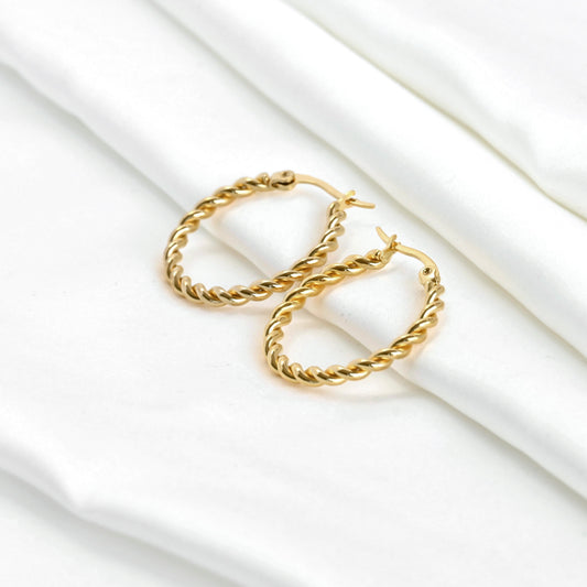 Gold thin twisted hoop earrings on a white fabric background