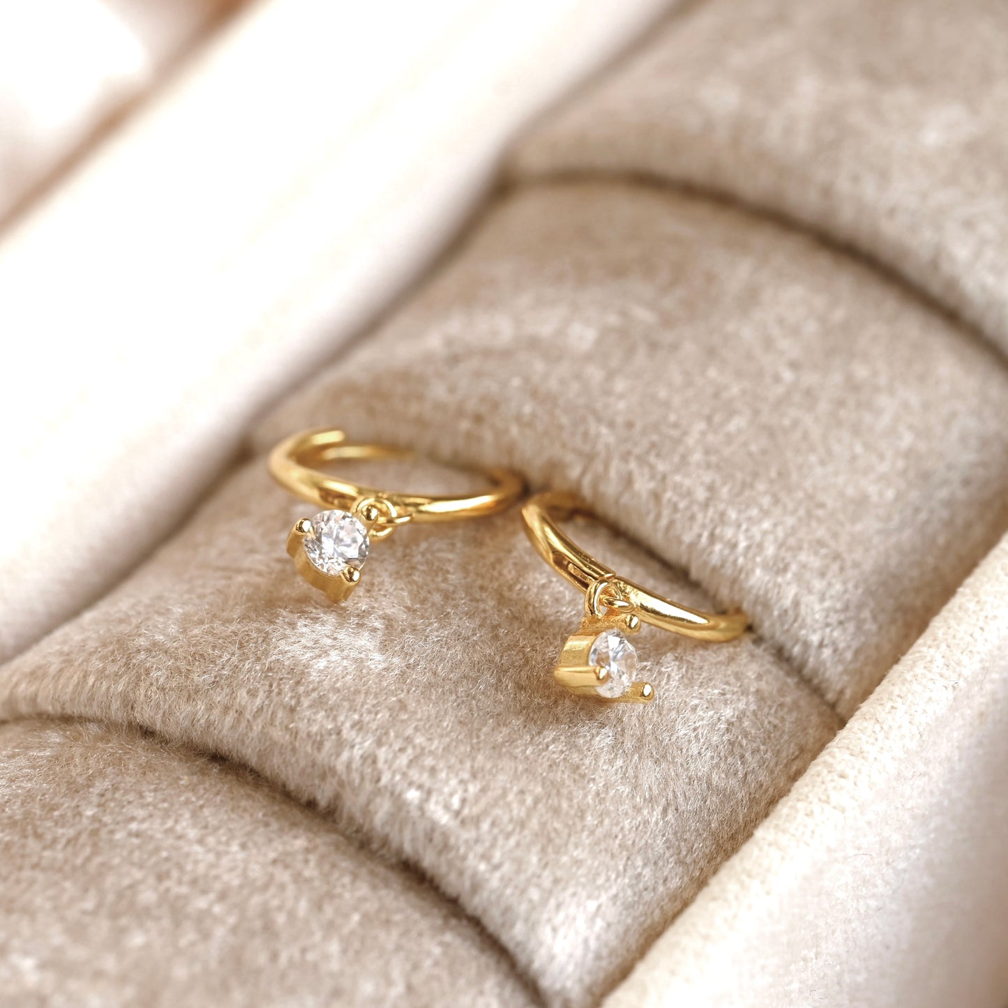 Two small gold hoop earings with diamonds on a beige jewelry box.