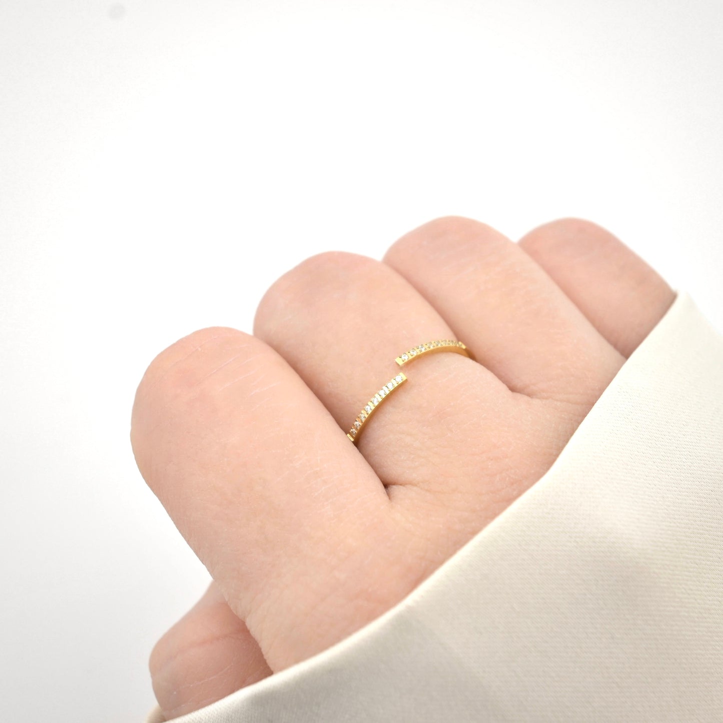 Thin gold bypass ring on a finger against a white background