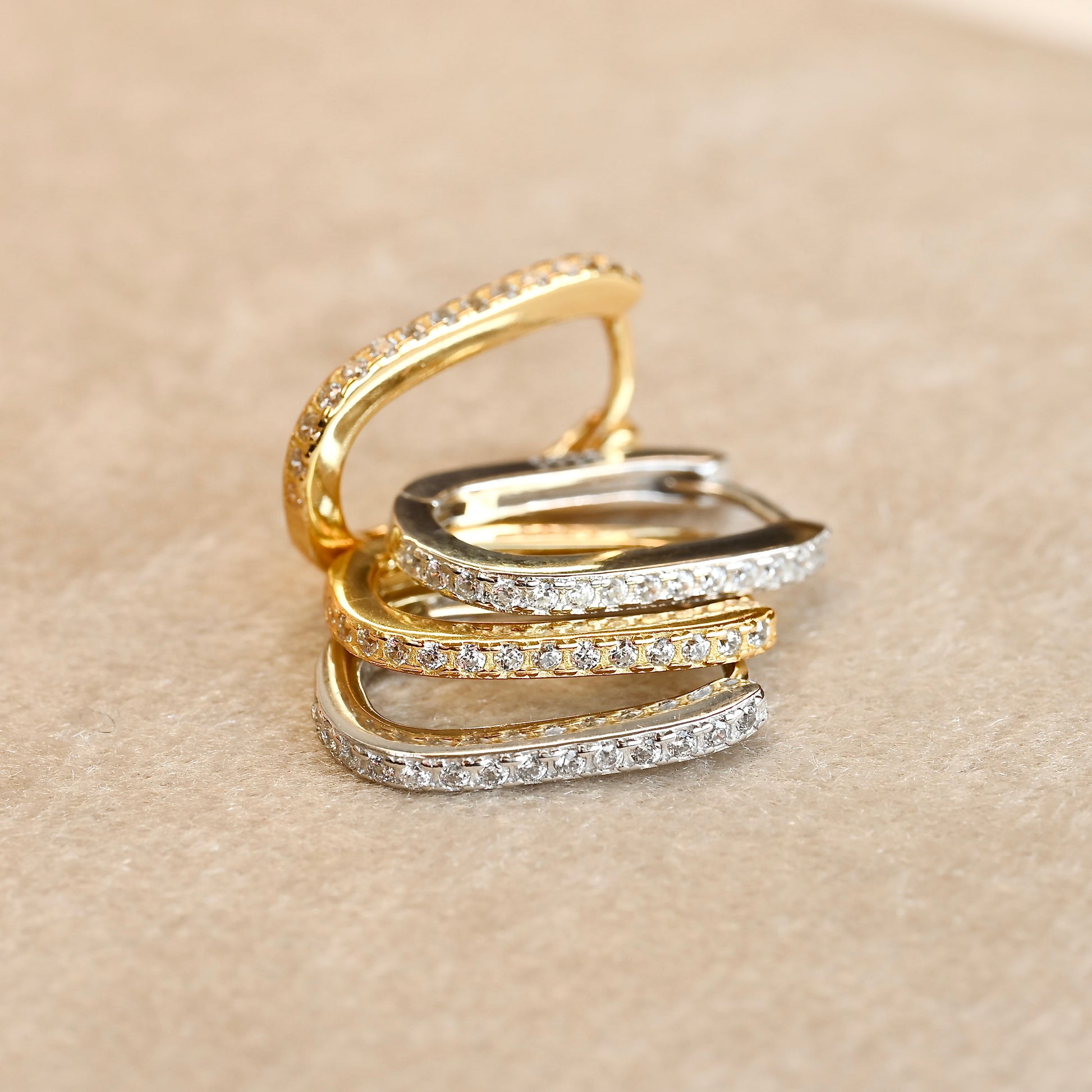 Set of gold and silver U earrings with pave set diamonds stacked on top of each other on a beige background