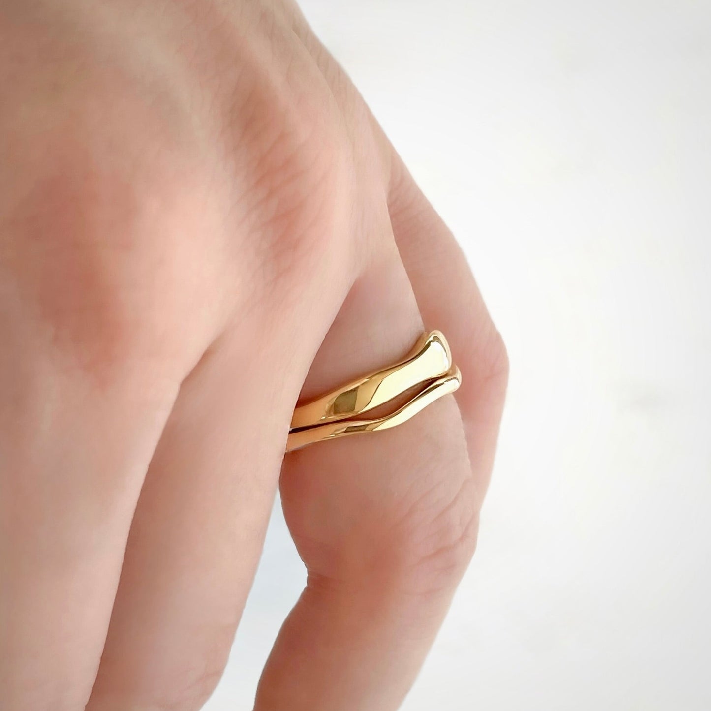 Stacked gold rings with organic shape, one wide and one thin, on person's hand against white background