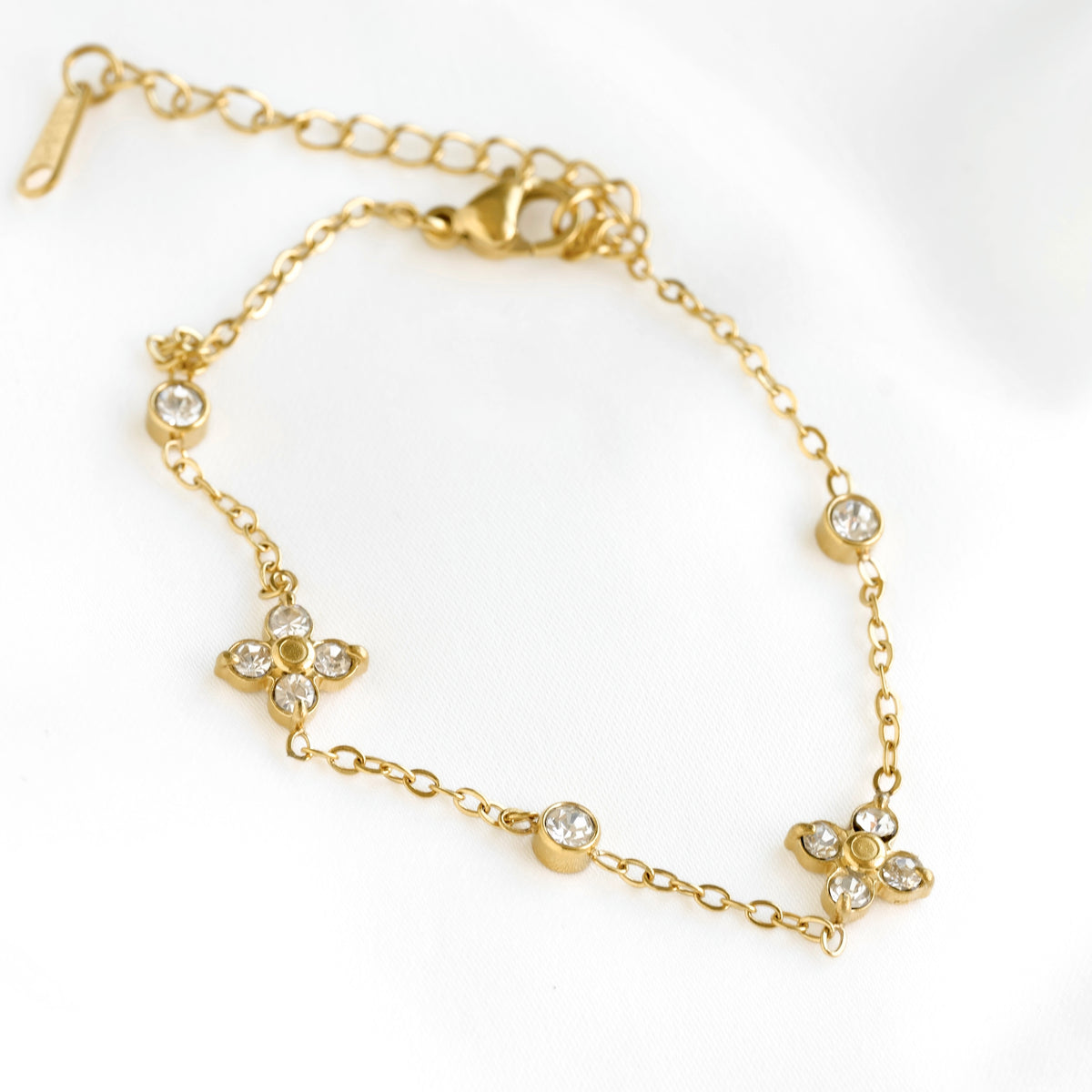 A delicate gold chain bracelet featuring three floral motifs set with clear rhinestones, displayed on a clean white background.