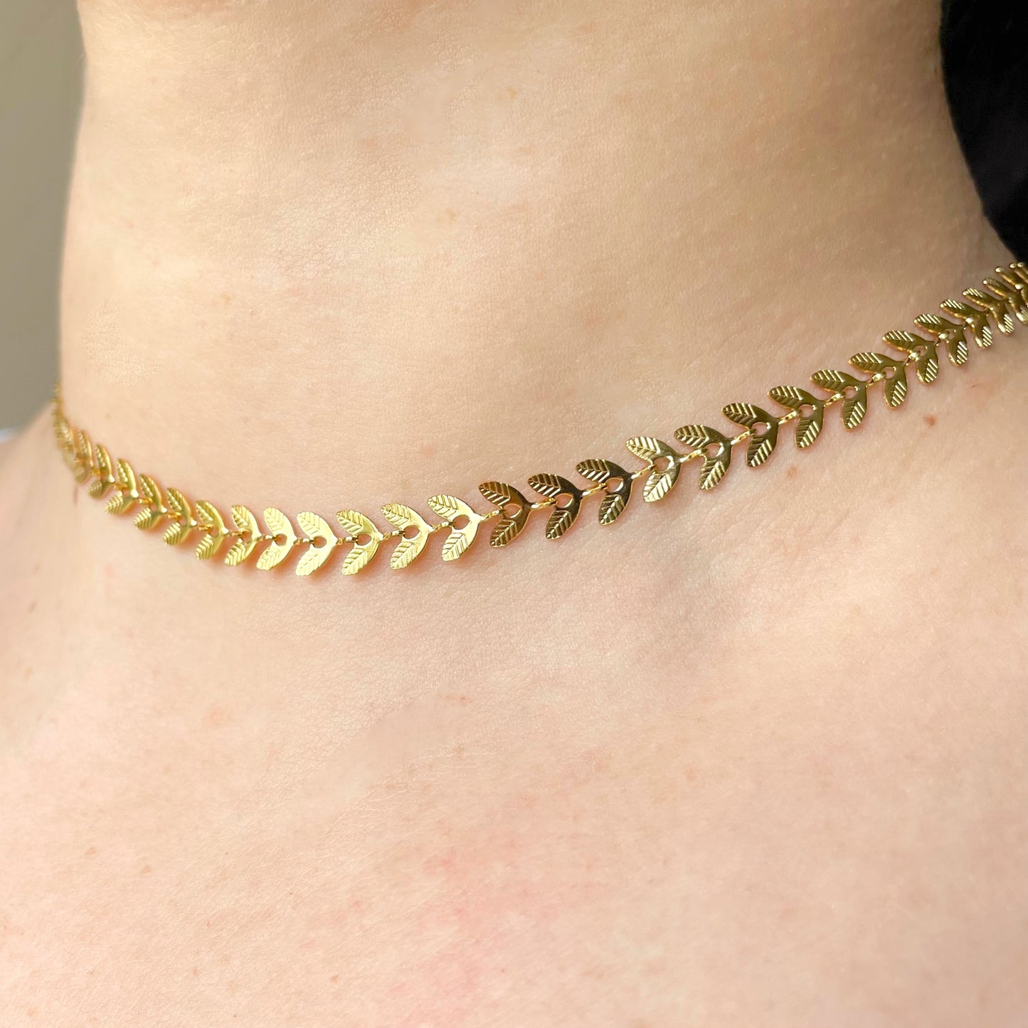 Close-up view of gold leaf choker necklace on a person's neck with a neutral background