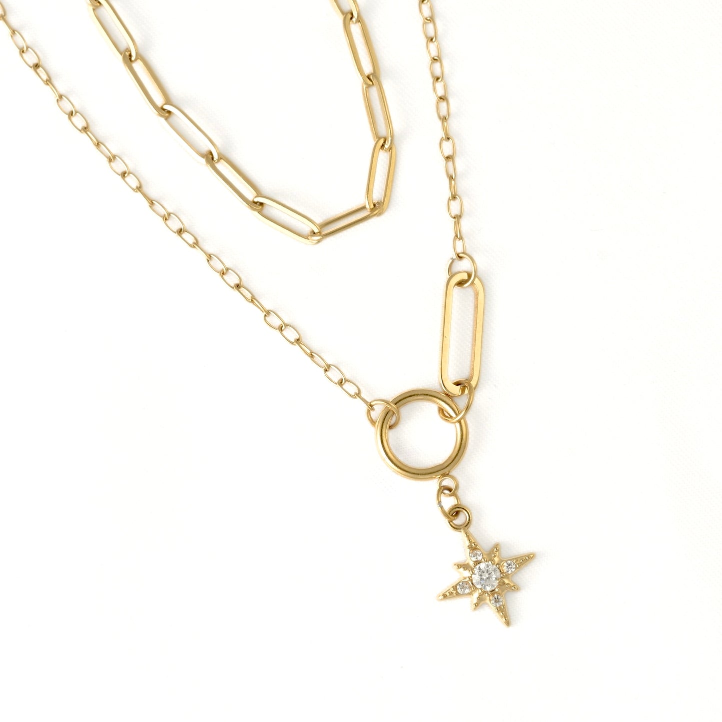 A gold layered necklace featuring a paperclip chain and a longer chain with a ring connector and a dangling star charm set with small clear stones, shown on a plain white background.