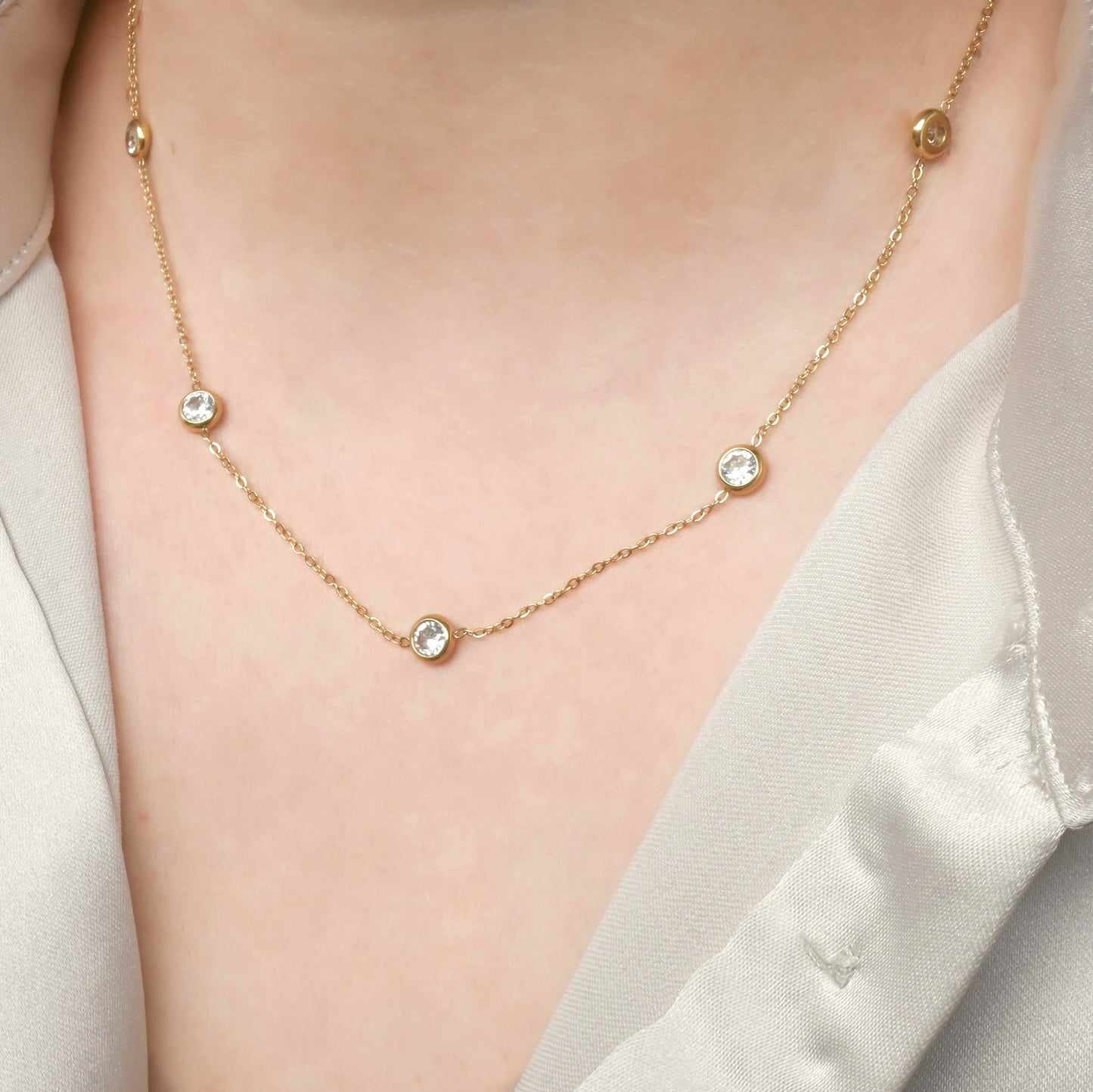Gold necklace with small bezel crystals on a person wearing a white shirt.