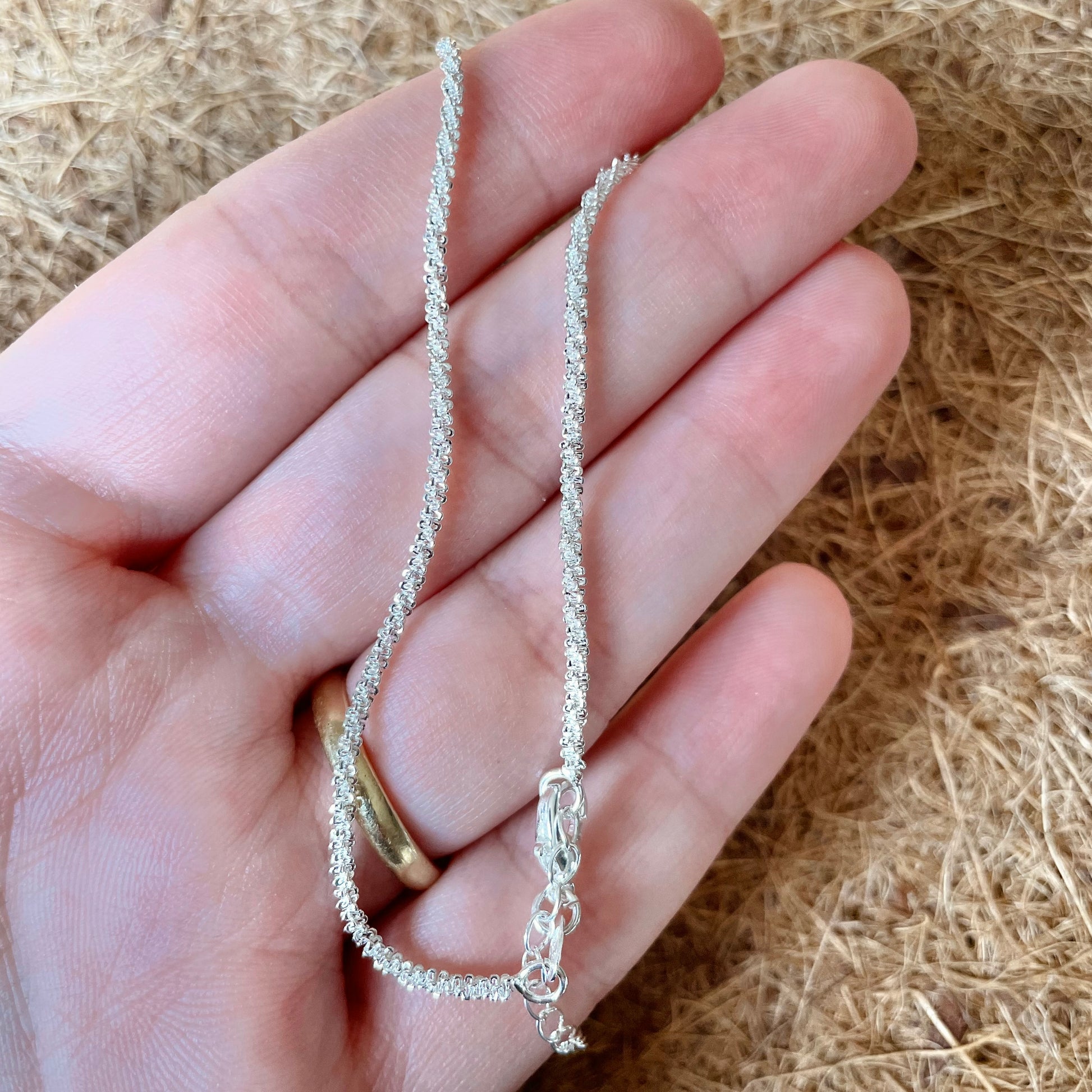 Silver ankle chain held in a hand against a natural background