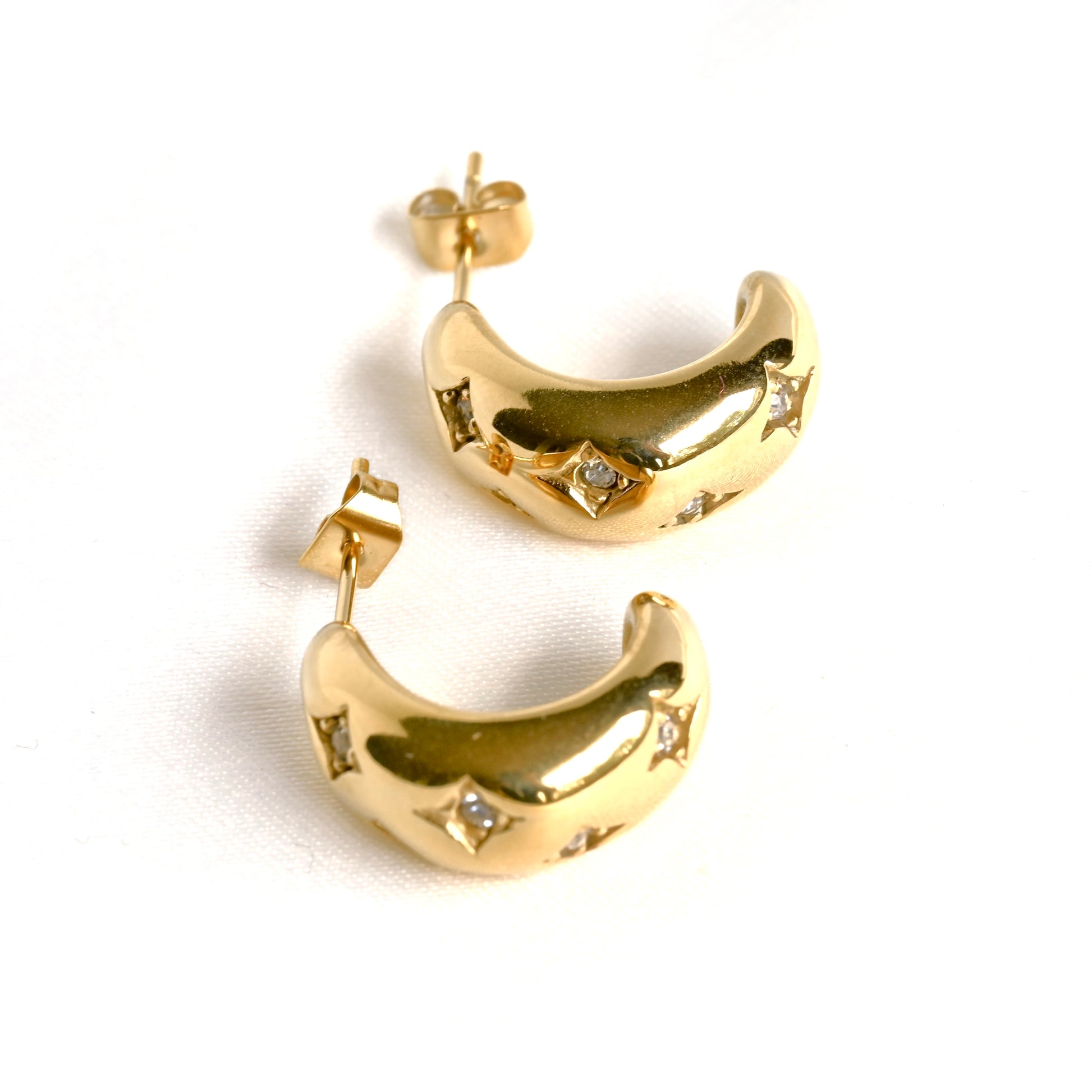  Top view of gold C hoops with small clear diamonds, posts and butterfly backs on a white background