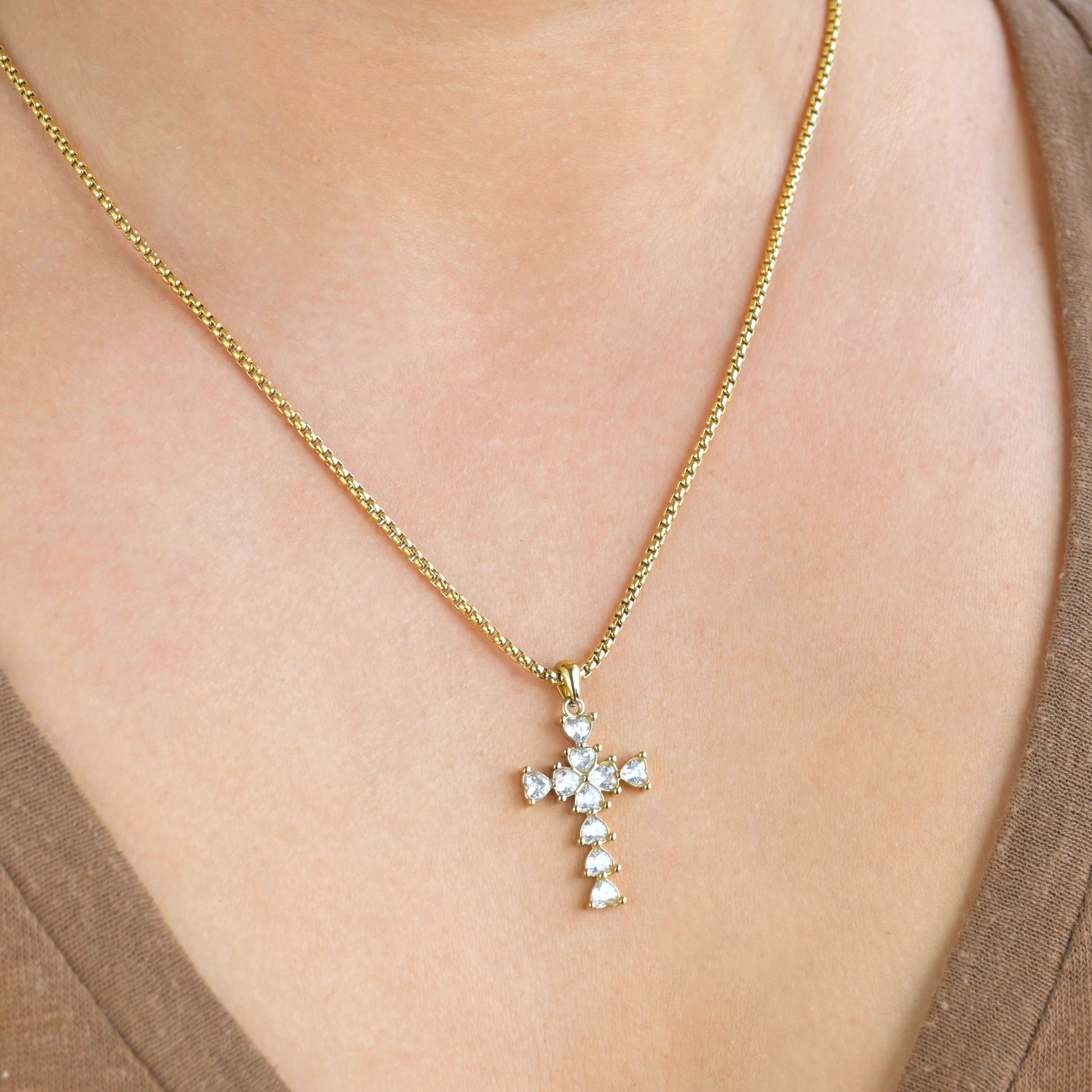 Diamond Gold necklace with a cross pendant on a person wearing a brown top.