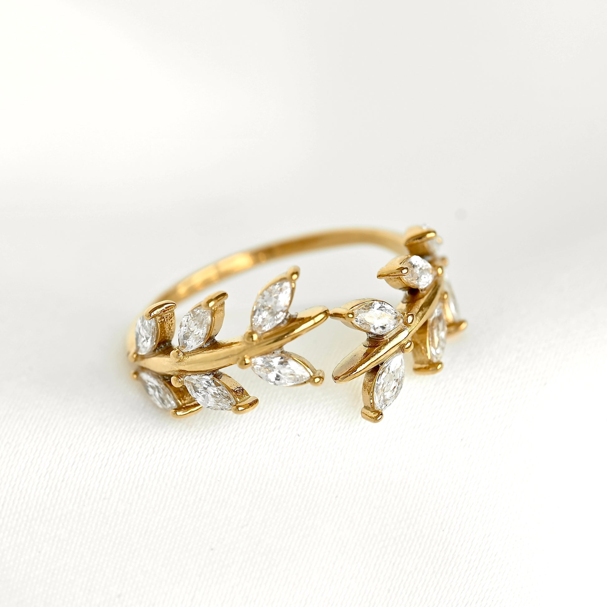 A gold leaf ring featuring marquise-cut clear gemstones, photographed on a clean white textured fabric background.