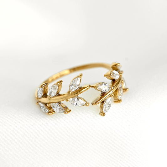 A gold leaf ring featuring marquise-cut clear gemstones, photographed on a clean white textured fabric background.