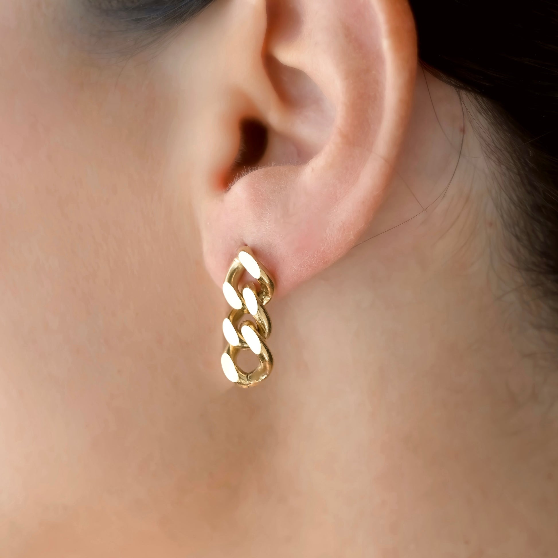 Gold chain earring worn by a person form a close up angle