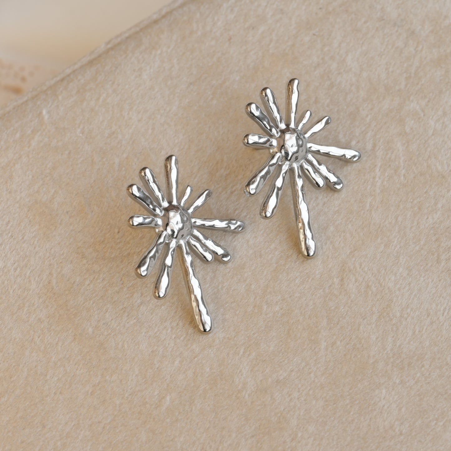 Silver sun earrings on a beige surface