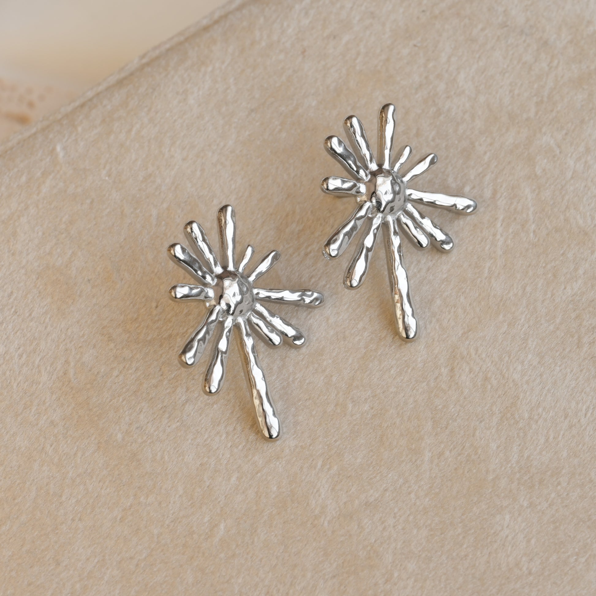 Silver sun earrings on a beige surface