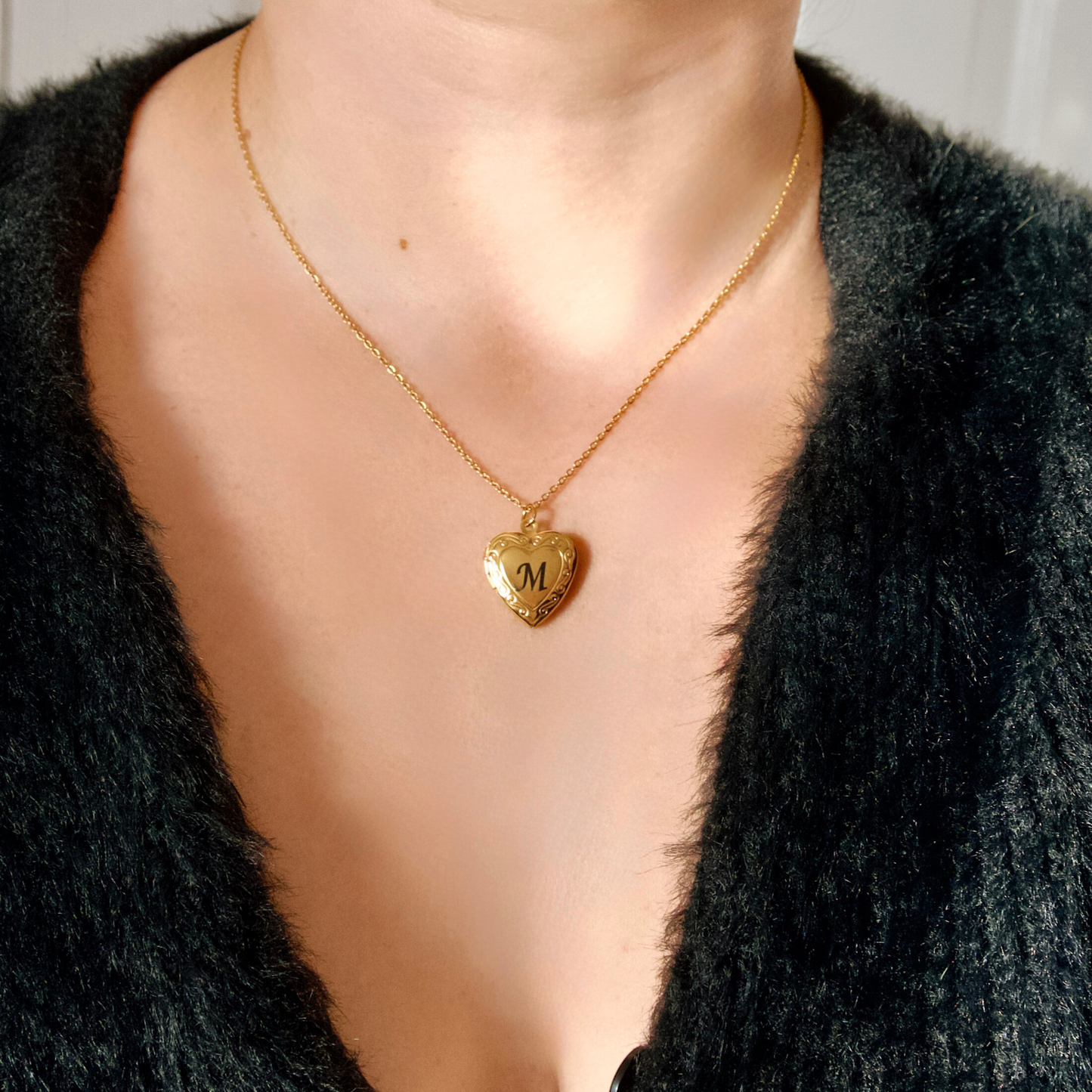 front view of gold heart necklace with initial 'M' worn by a person in a black cardigan.