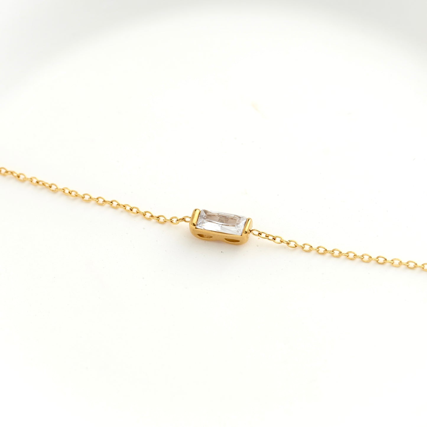 A delicate gold chain bracelet featuring a small rectangular bezel-set clear gemstone at the center, displayed on a clean white background.