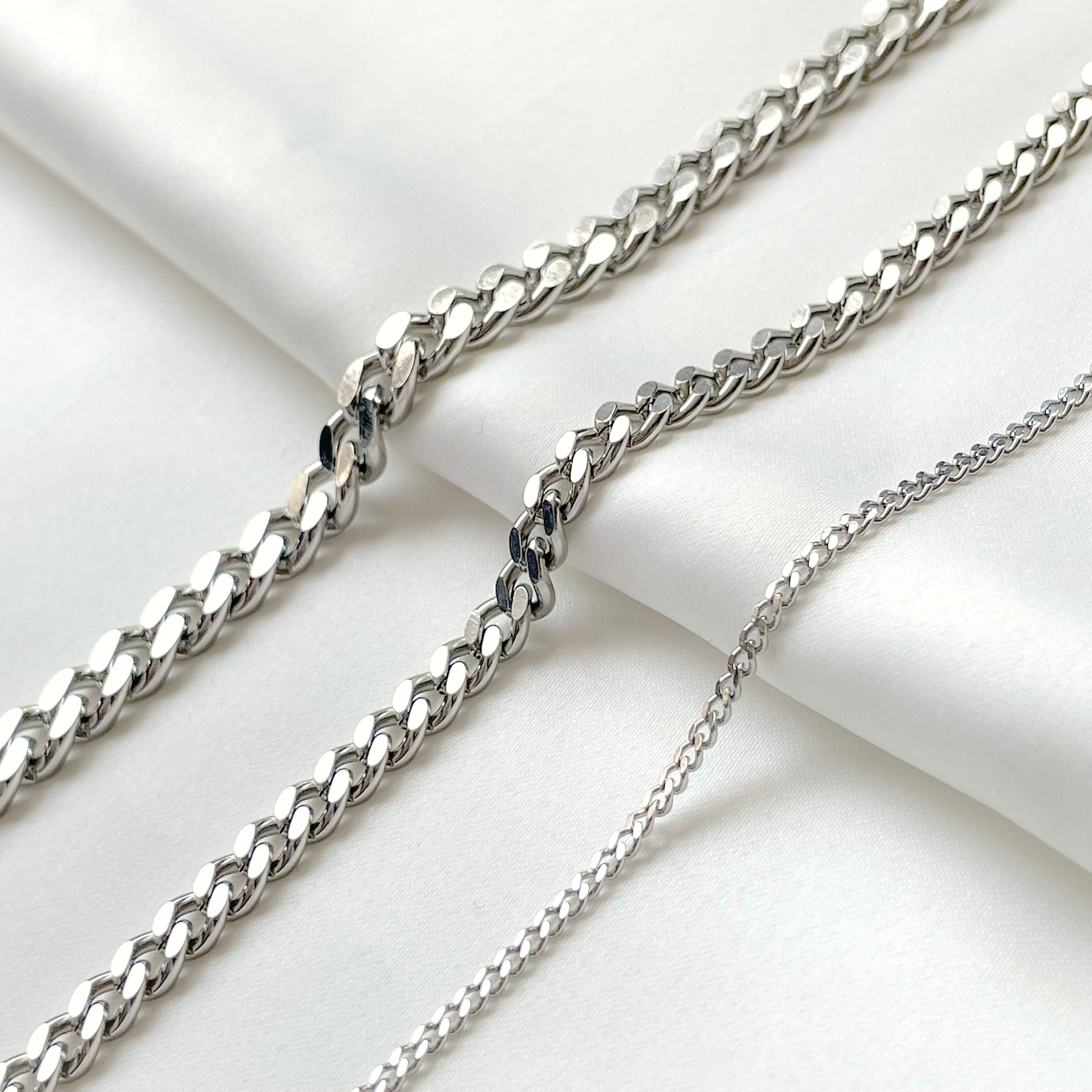 Three silver chains of different thicknesses on a light background