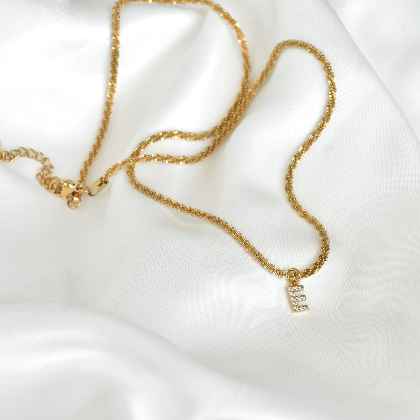Gold sparkle rope necklace with a small letter pendant on a white fabric background