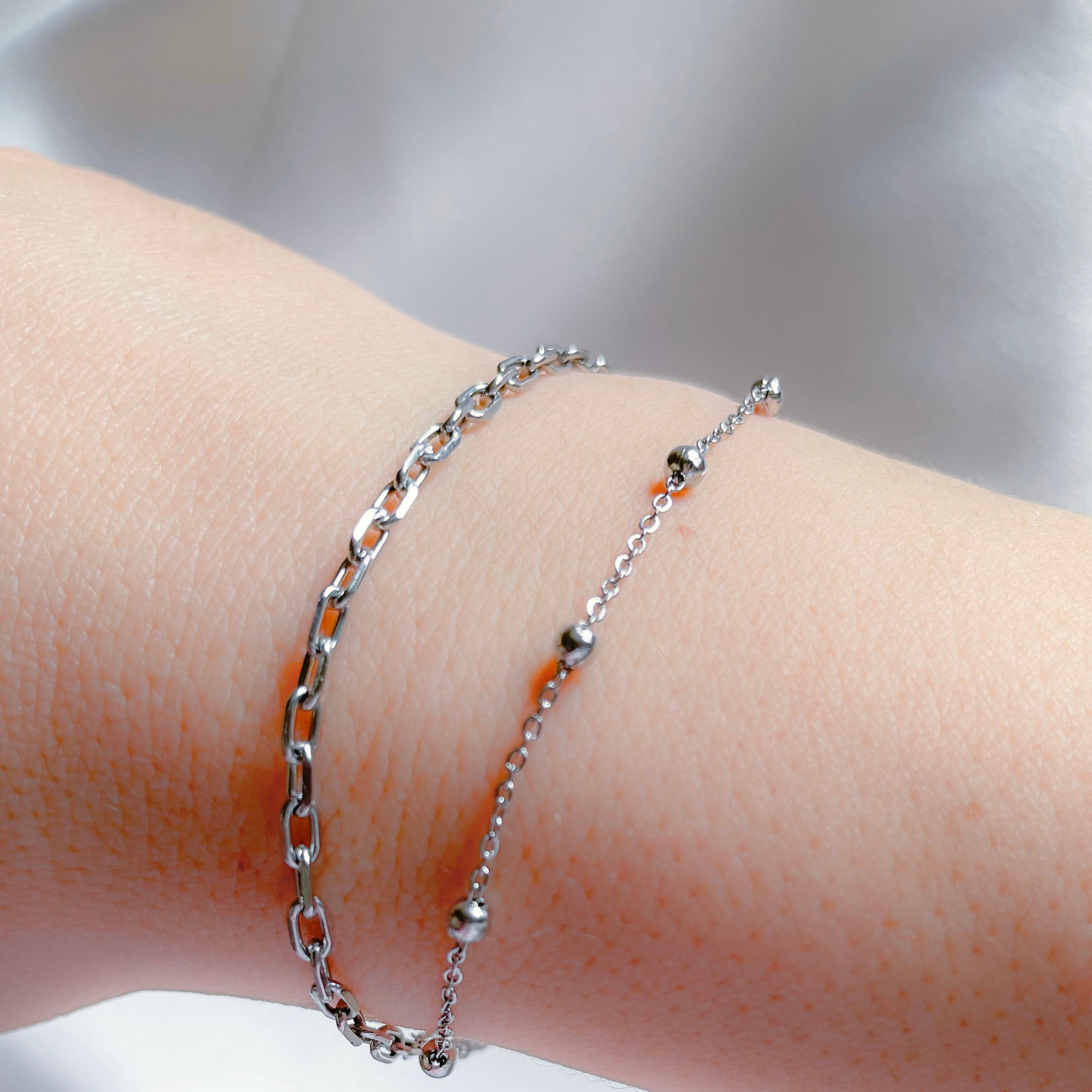 Silver chain bracelet set with a satellite chain and dainty paperclip chain on a wrist with a blurred background