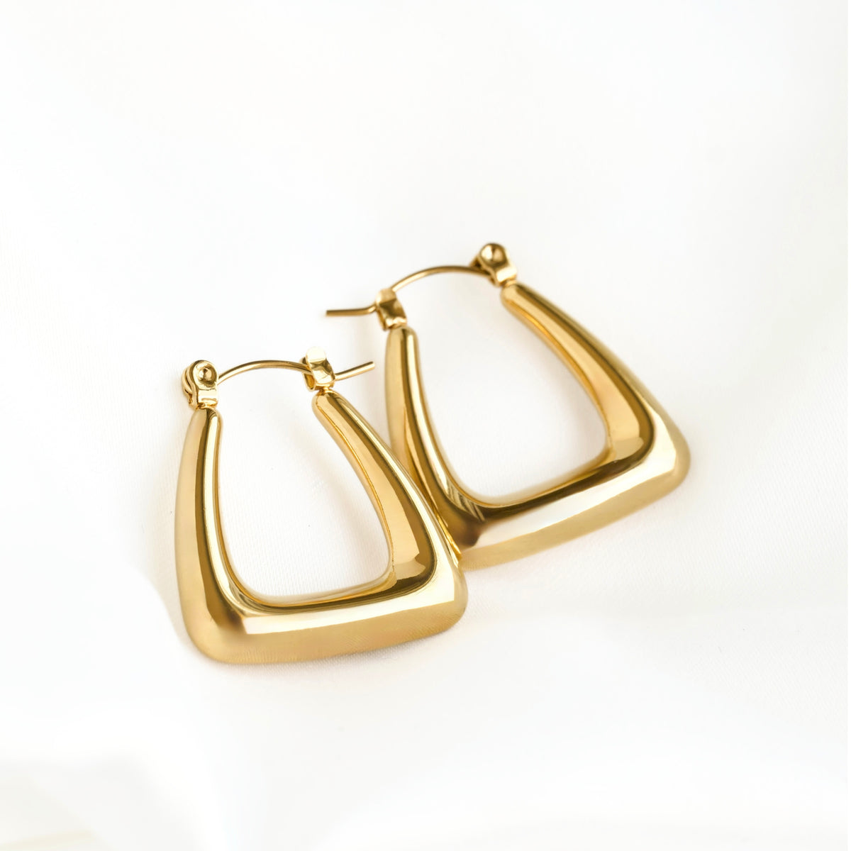 A pair of polished gold-tone geometric hoop earrings with a thick, rounded triangular frame design, displayed on a clean white background.