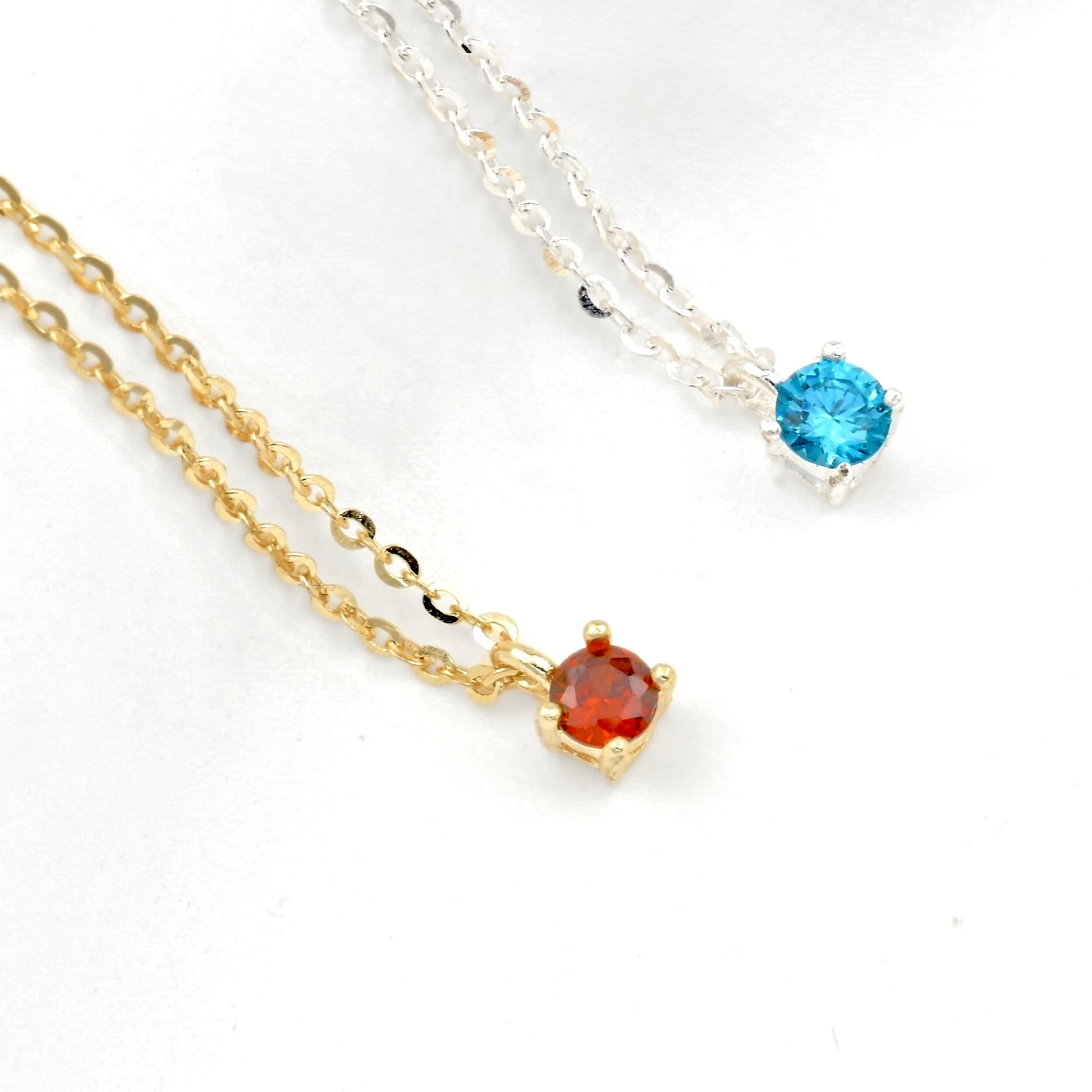 Two necklaces, one gold and one silver with a single gemstone on each on a white background