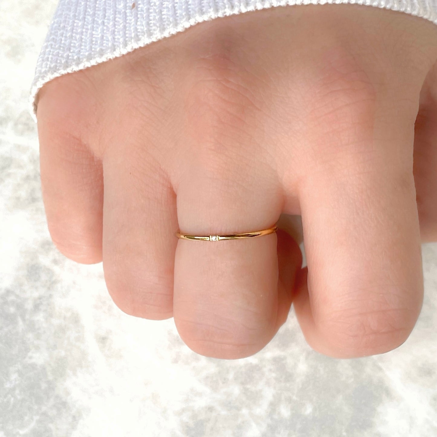 Top view of ultra slim gold ring with a single CZ stone on a finger against a white background
