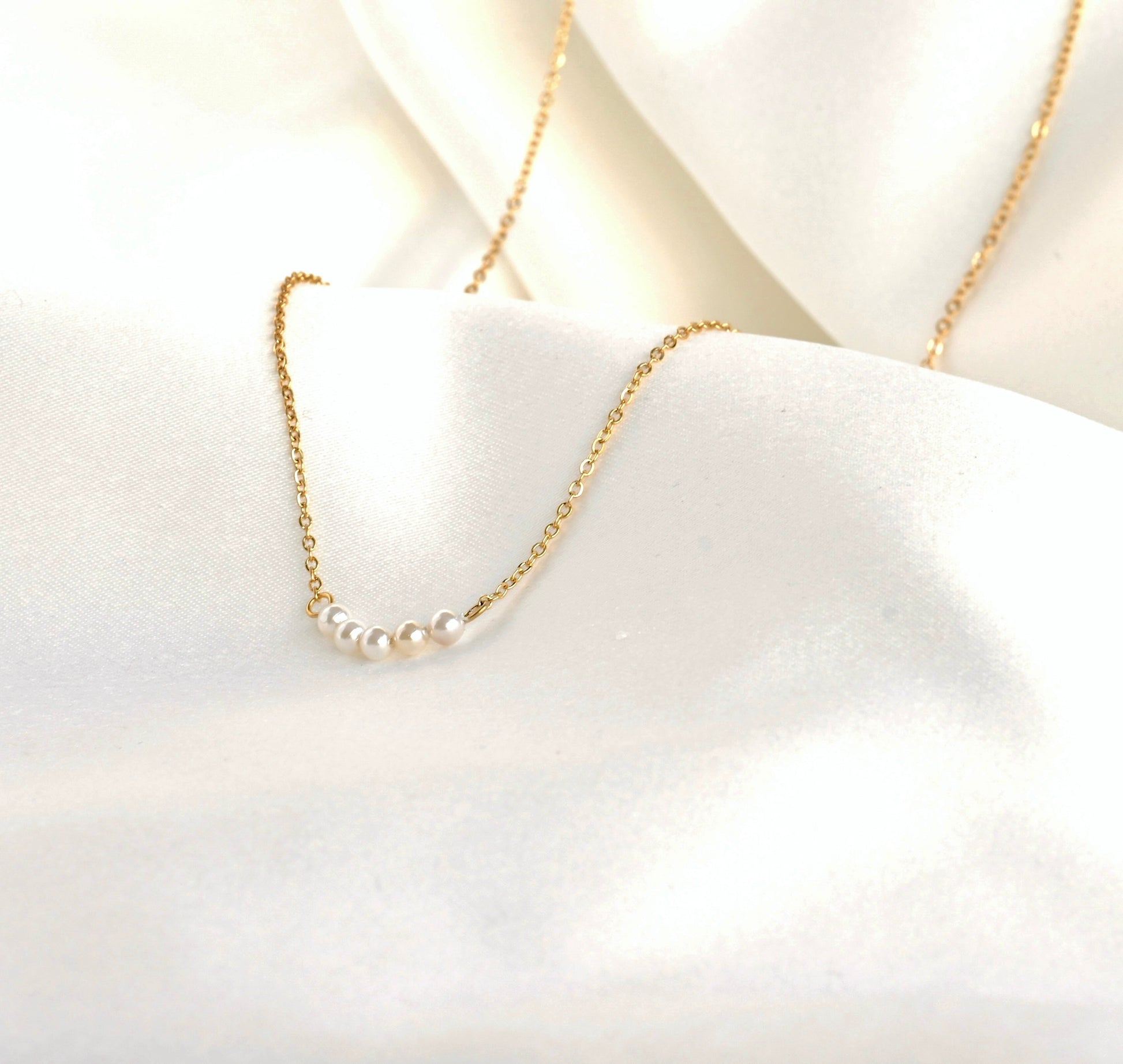 Gold necklace with tiny pearls on a white fabric background