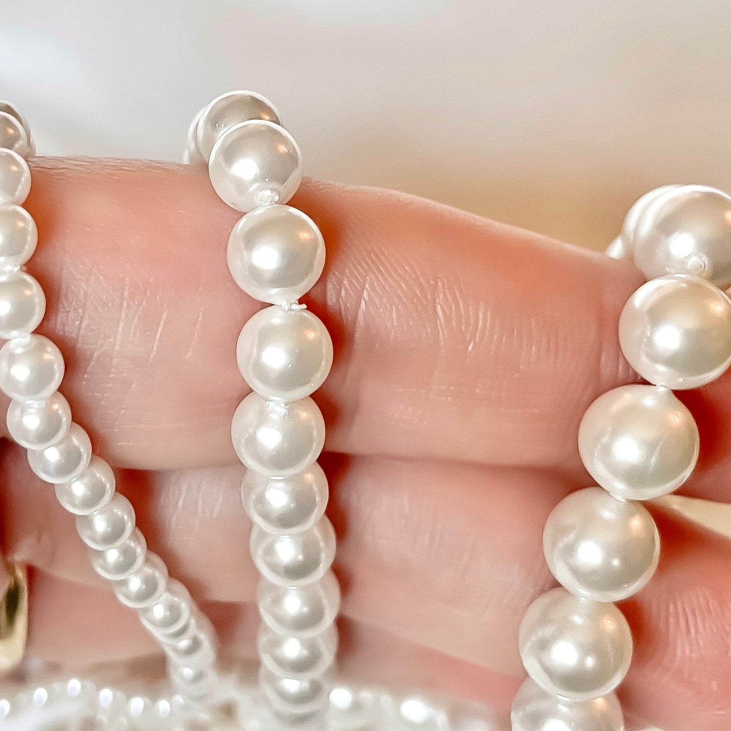 Close-up of a hand holding  pearl necklaces with three different size pearls with a blurred background