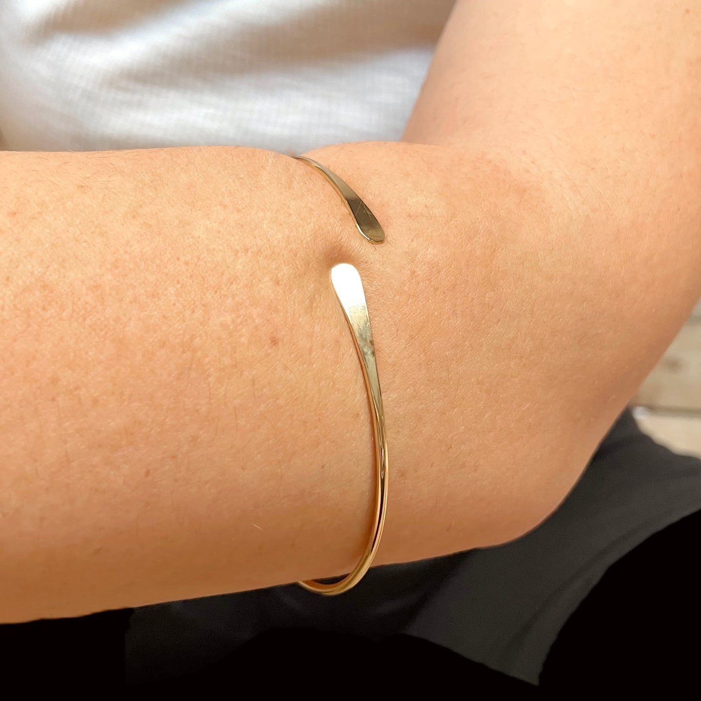 Close-up view of open gold bangle on a person's forearm with a neutral background