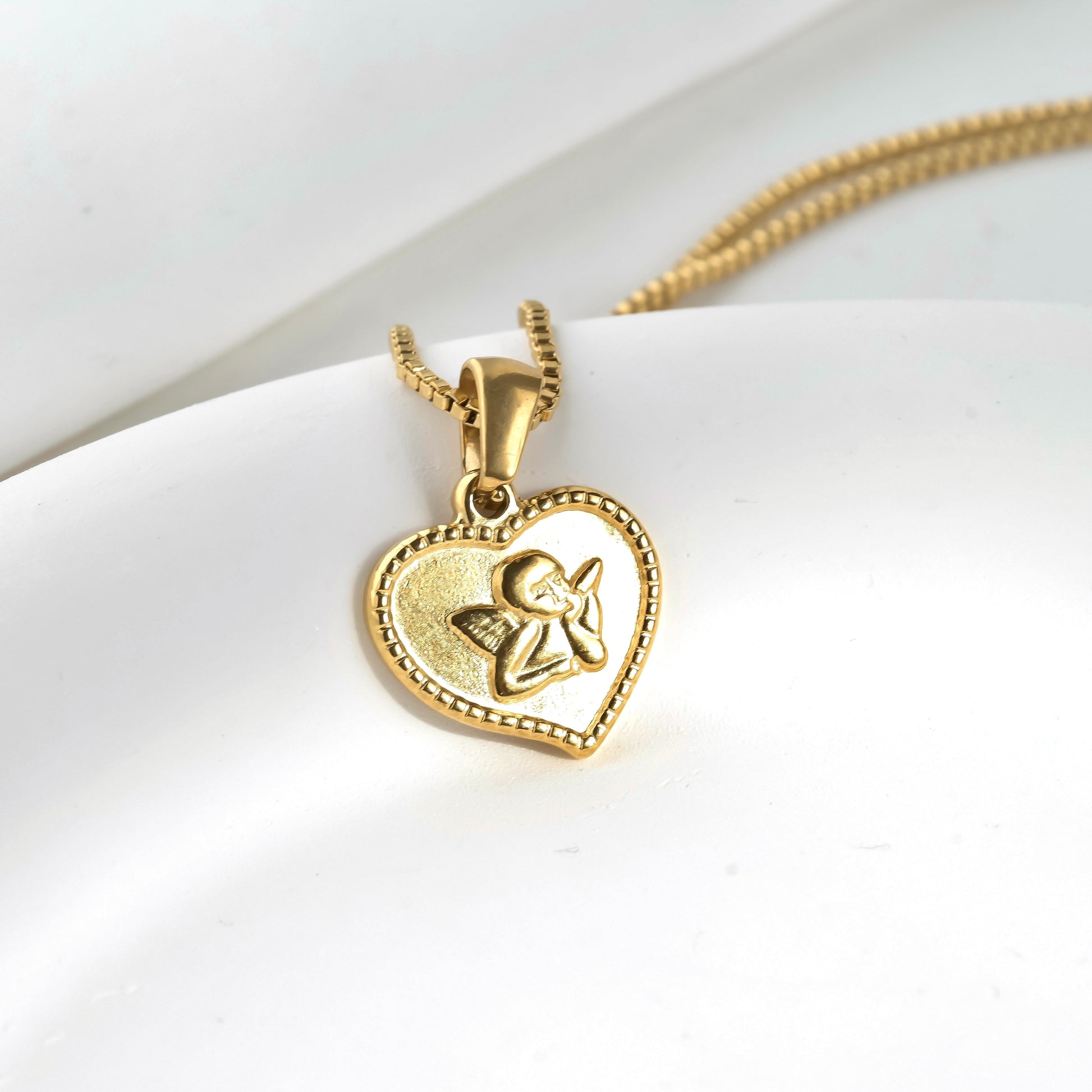 Gold milgrain heart pendant with an angel design hanging from a thin box chain on a white background
