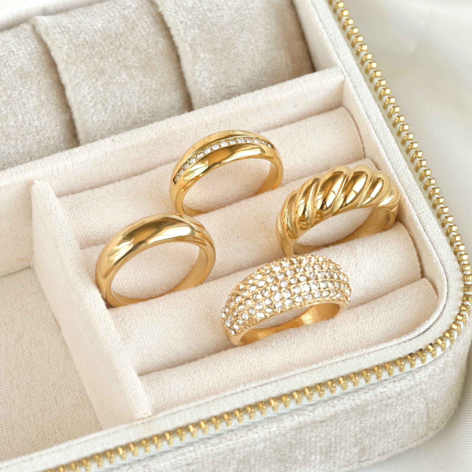 Set of thick gold statement rings, two of them with CZ accents in a jewelry box on a light background