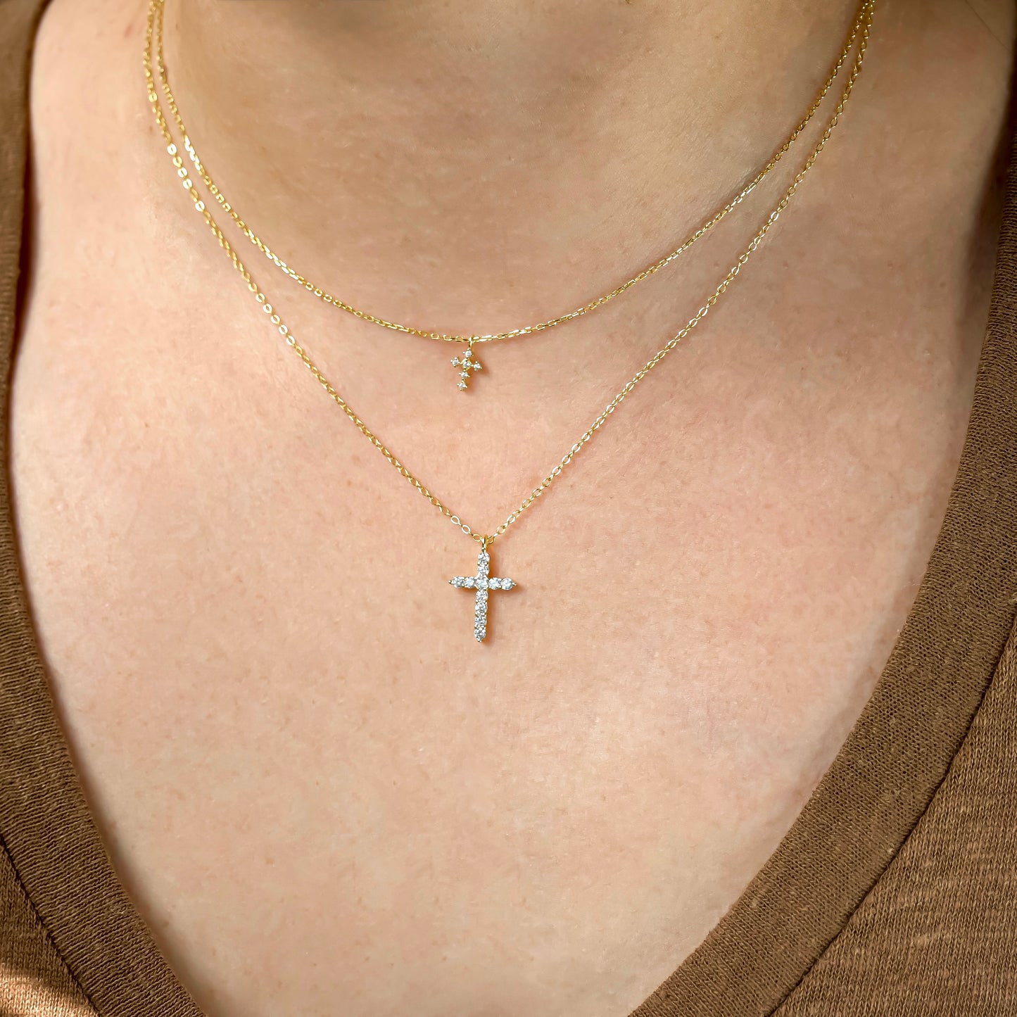 Close-up of a person wearing two gold necklaces, one super tiny and one small sized cross pendants.