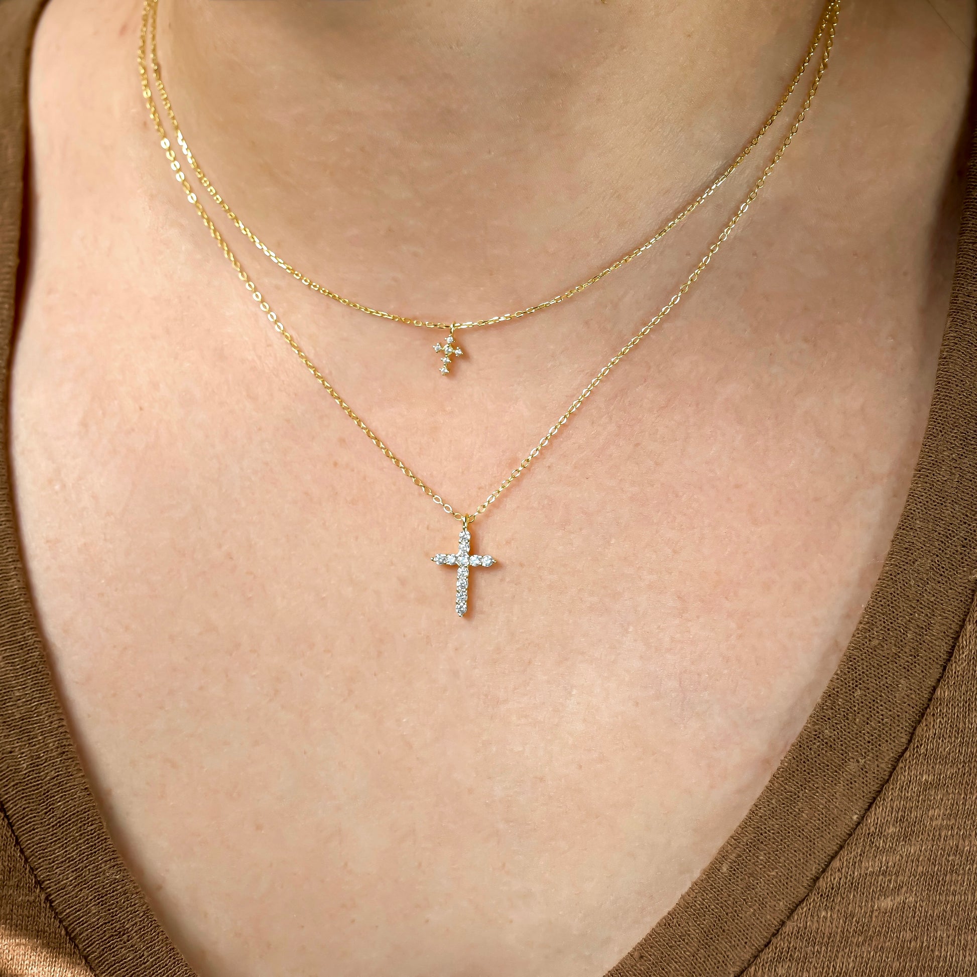 Close-up of a person wearing two gold necklaces, one super tiny and one small sized cross pendants.