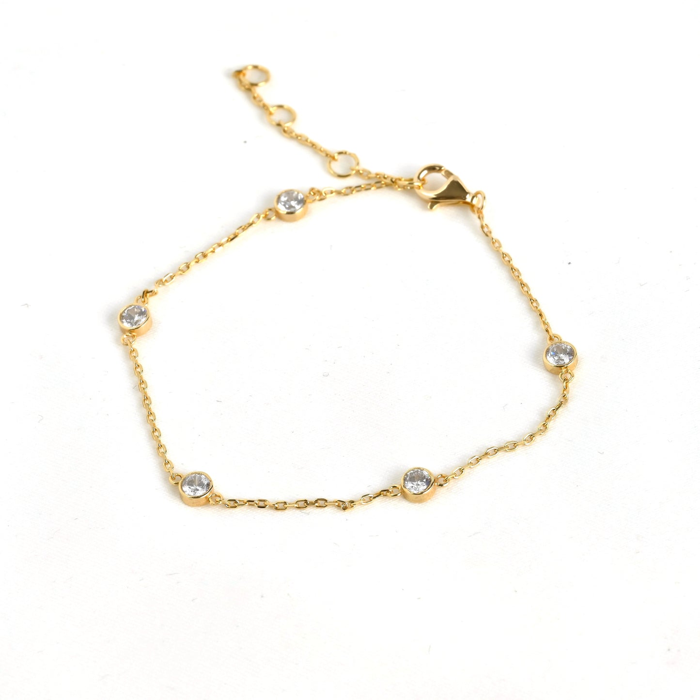 Delicate gold bezel station bracelet with small crystals and a three point extender on a white background