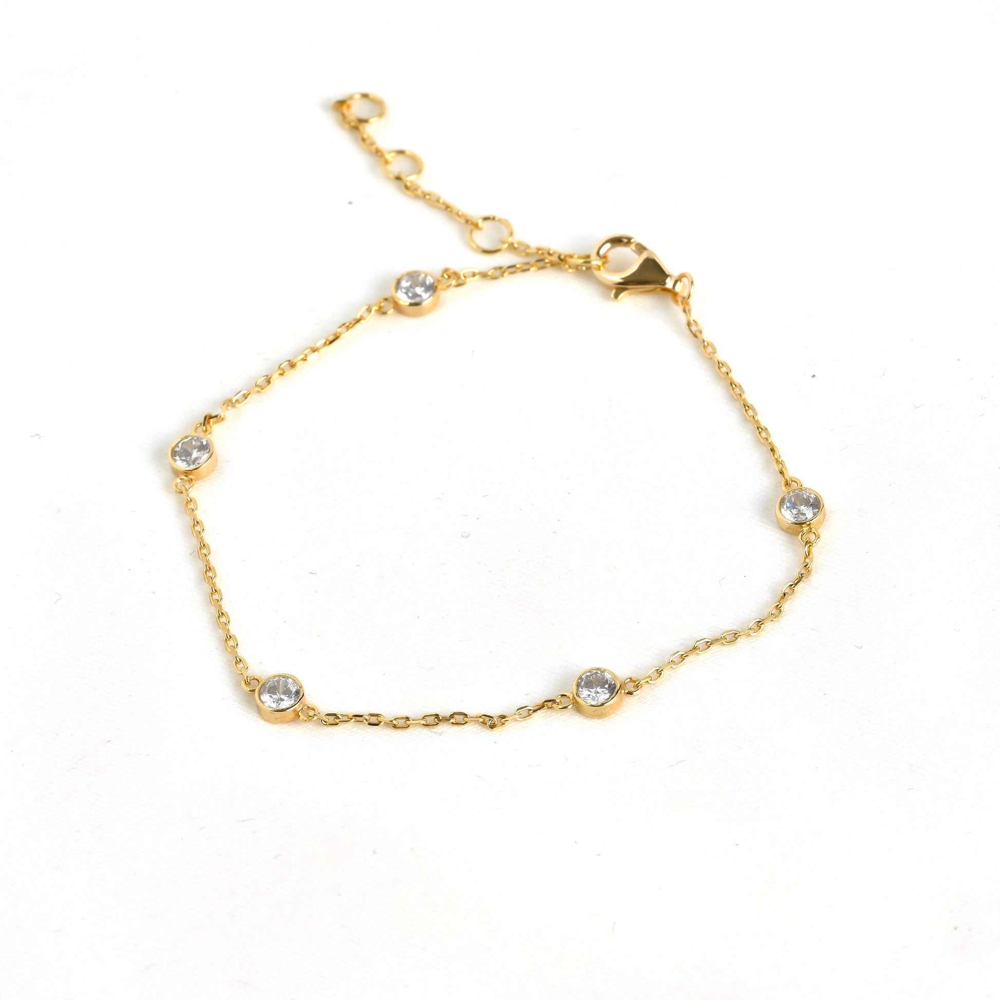 Delicate gold bezel station bracelet with small crystals and a three point extender on a white background