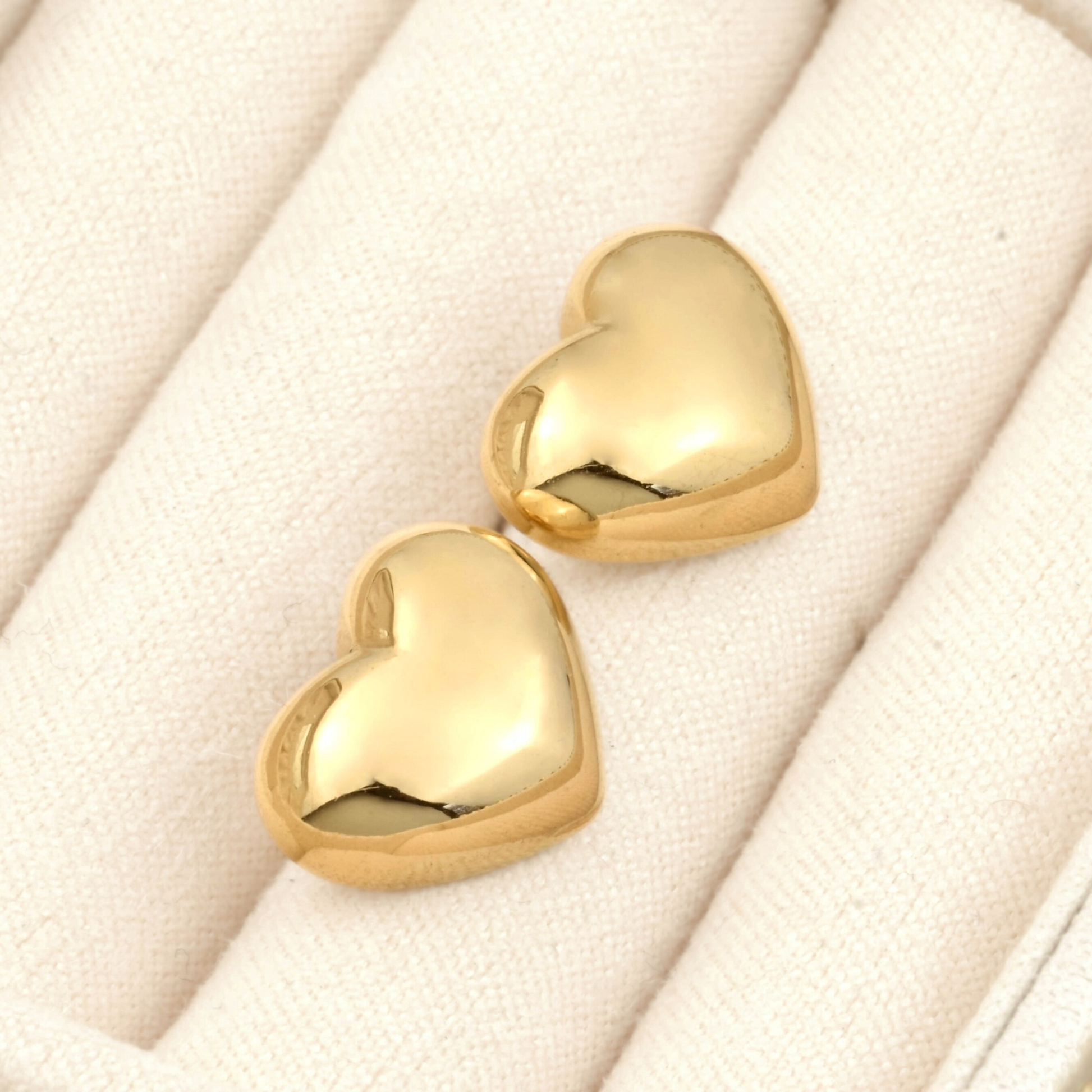 Puffy heart stud earrings on a soft beige fabric background