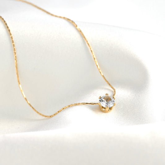 Gold solitaire necklace with a round CZ stone in a 6-prong basket setting and a delicate shimmering chain on a white background