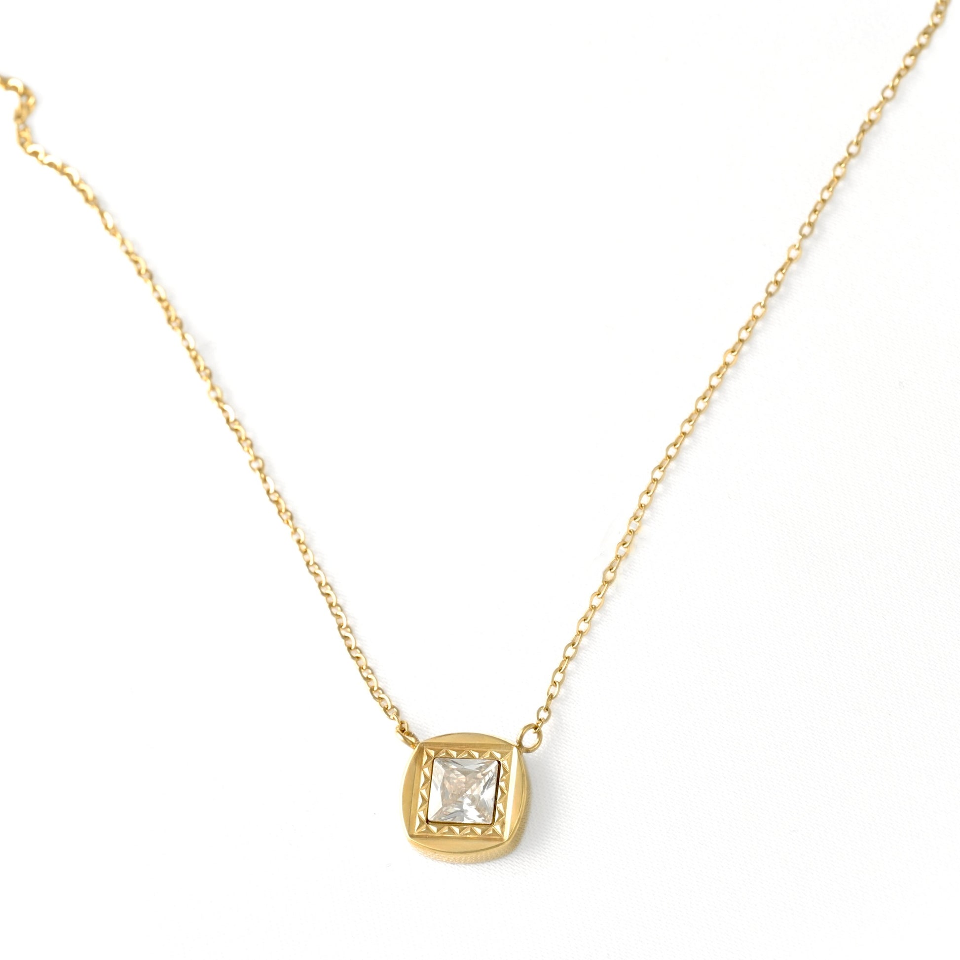 A delicate gold chain necklace with a small square bezel-set clear gemstone pendant, displayed on a clean white background.