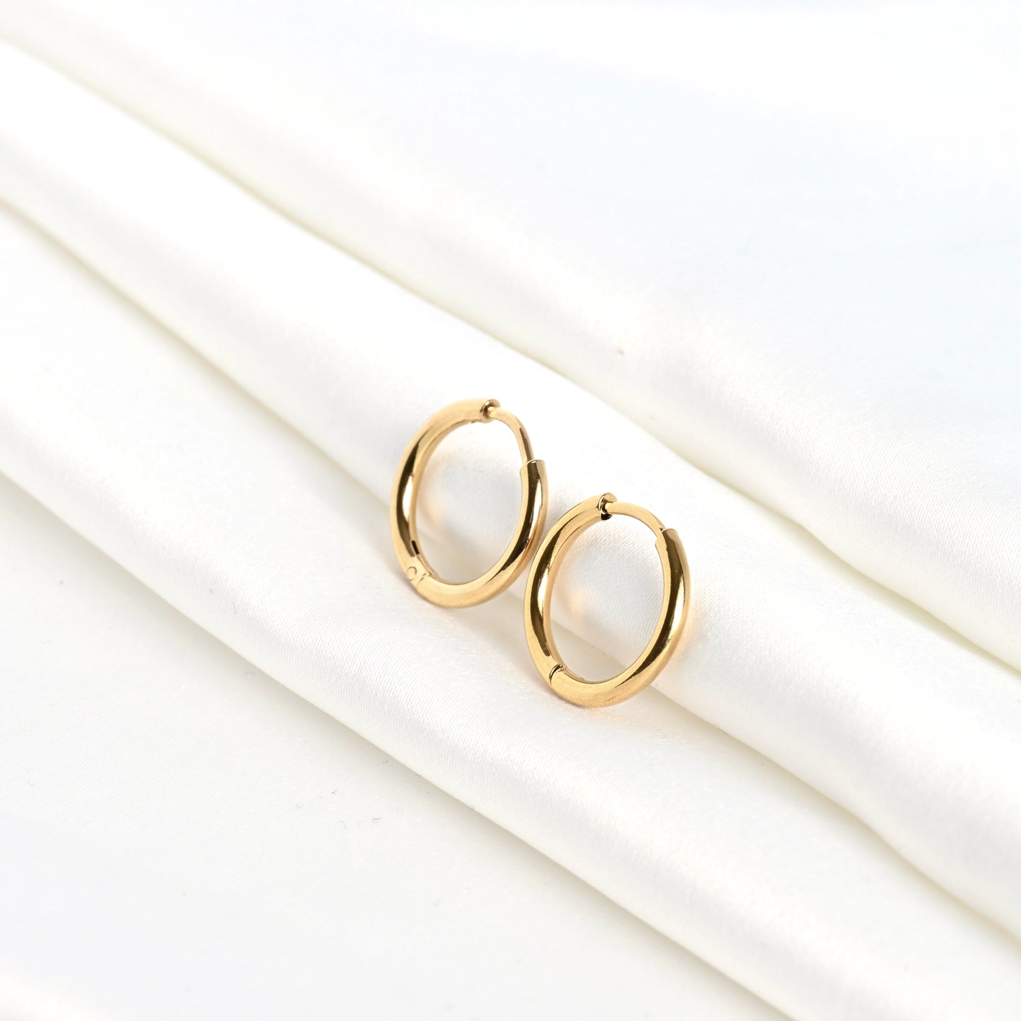 Small gold sleeper huggie earrings on a white satin fabric