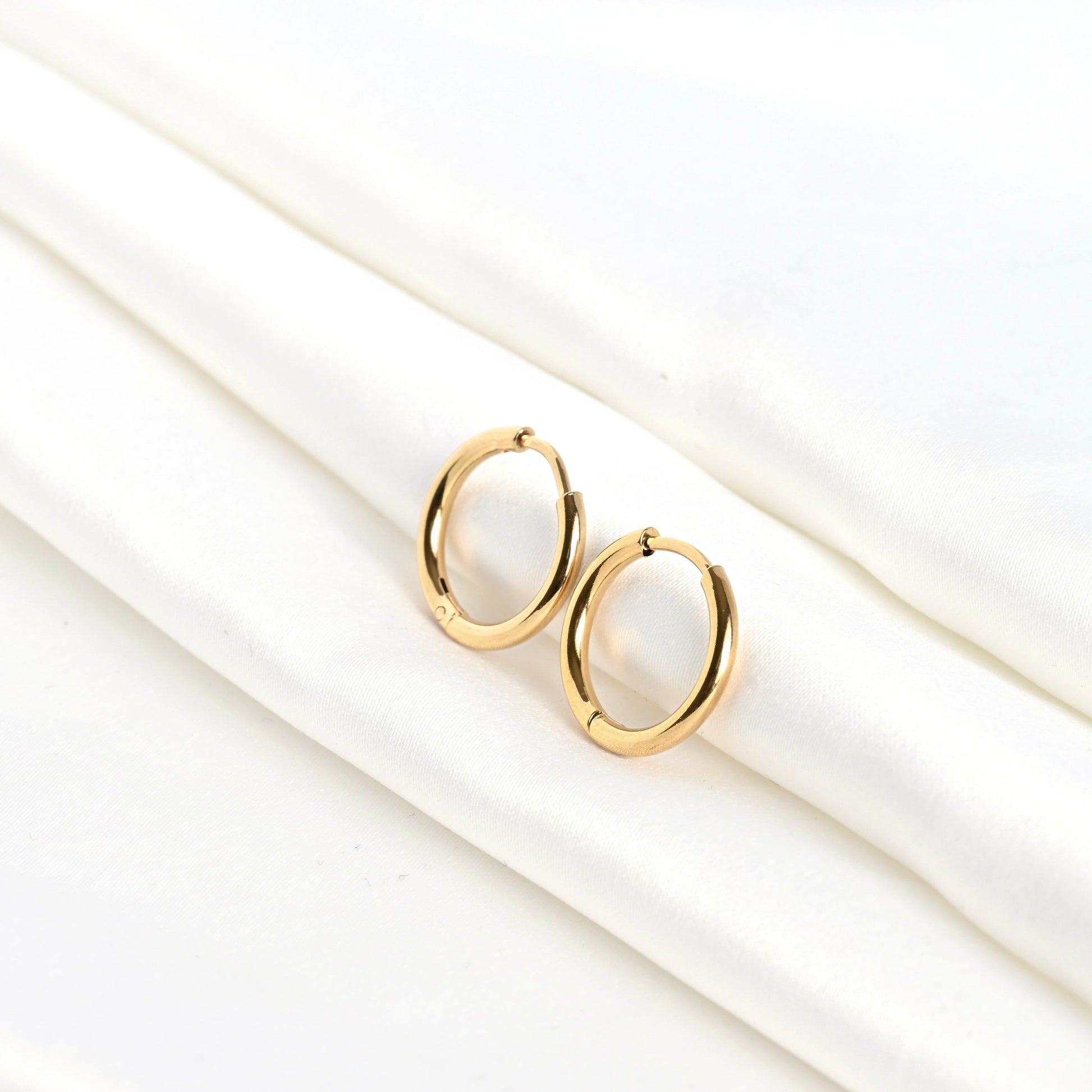 Small gold sleeper huggie earrings on a white satin fabric